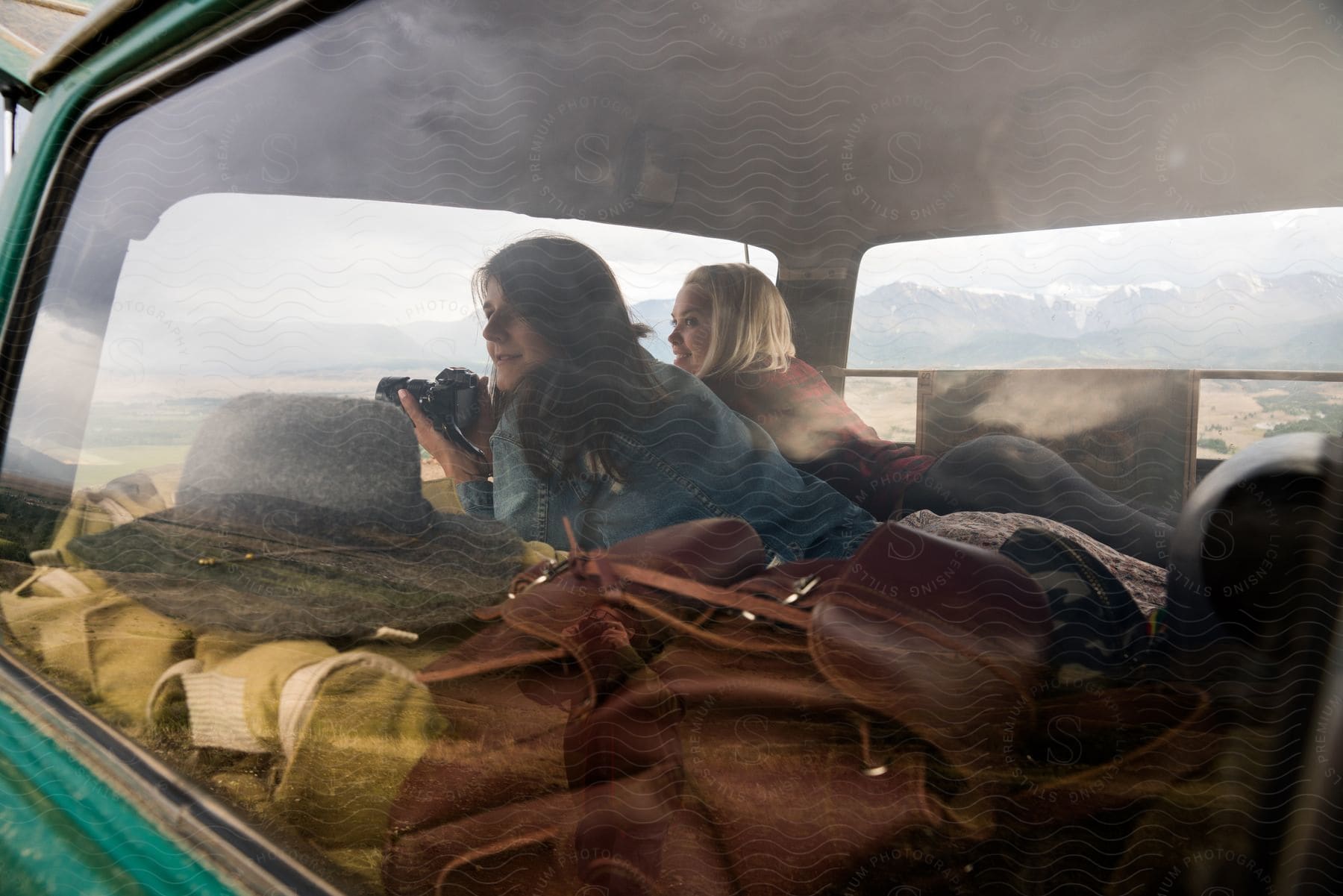 two young women lying down inside a car taking pictures of nature during day time