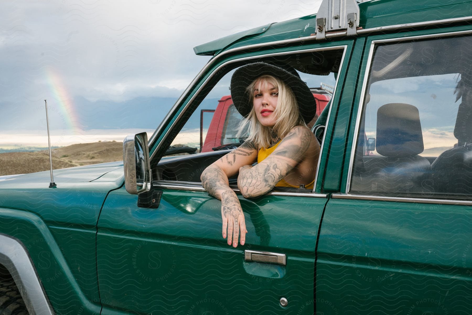 A young, blond woman sits in a green car and poses for the camera.