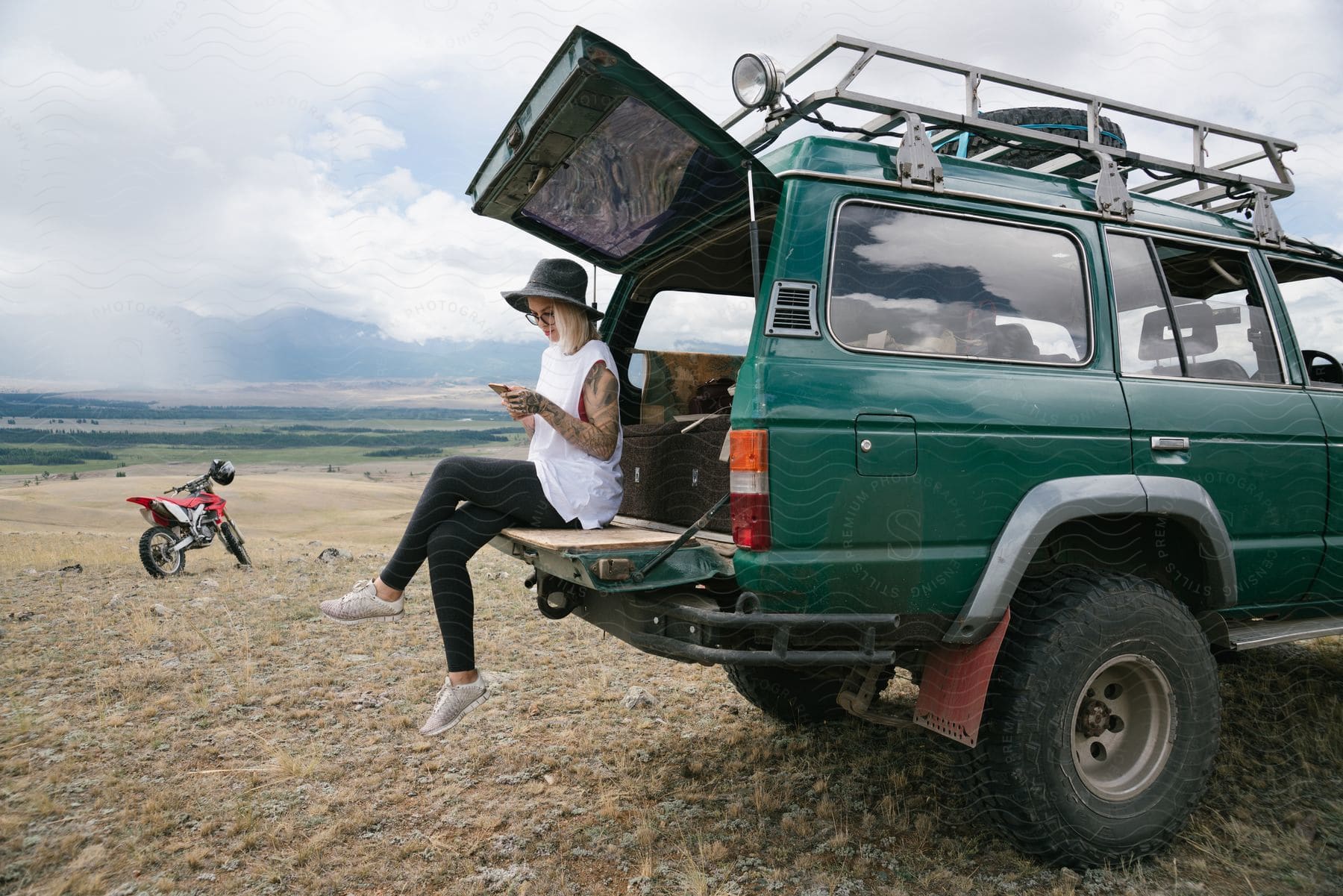 Stock photo of a young, blond woman is sitting on the tailgate of an suv while checking her smartphone.