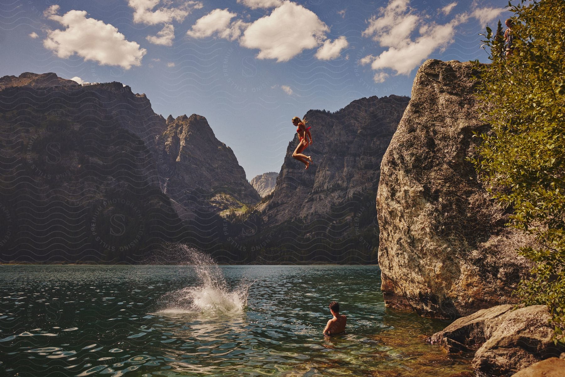 Teens having fun jumping in a mountain lake from a rocky cliff.