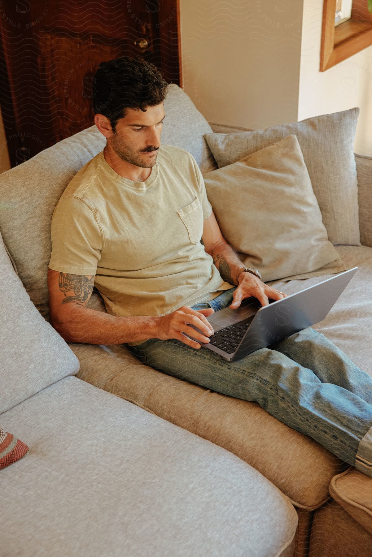 Man sitting on the sofa with legs extended, working on a laptop.