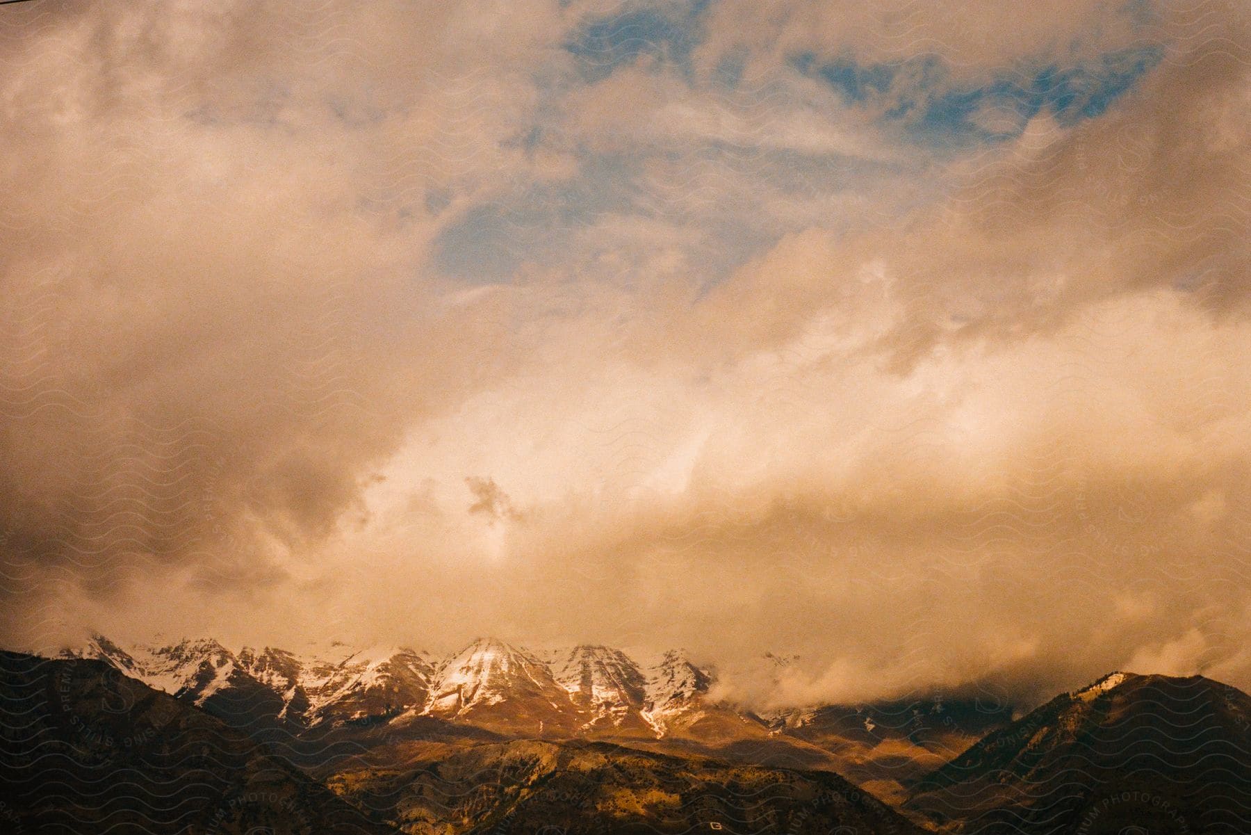 Mountains are having some snow covering as the pile of clouds are covering the blue sky.