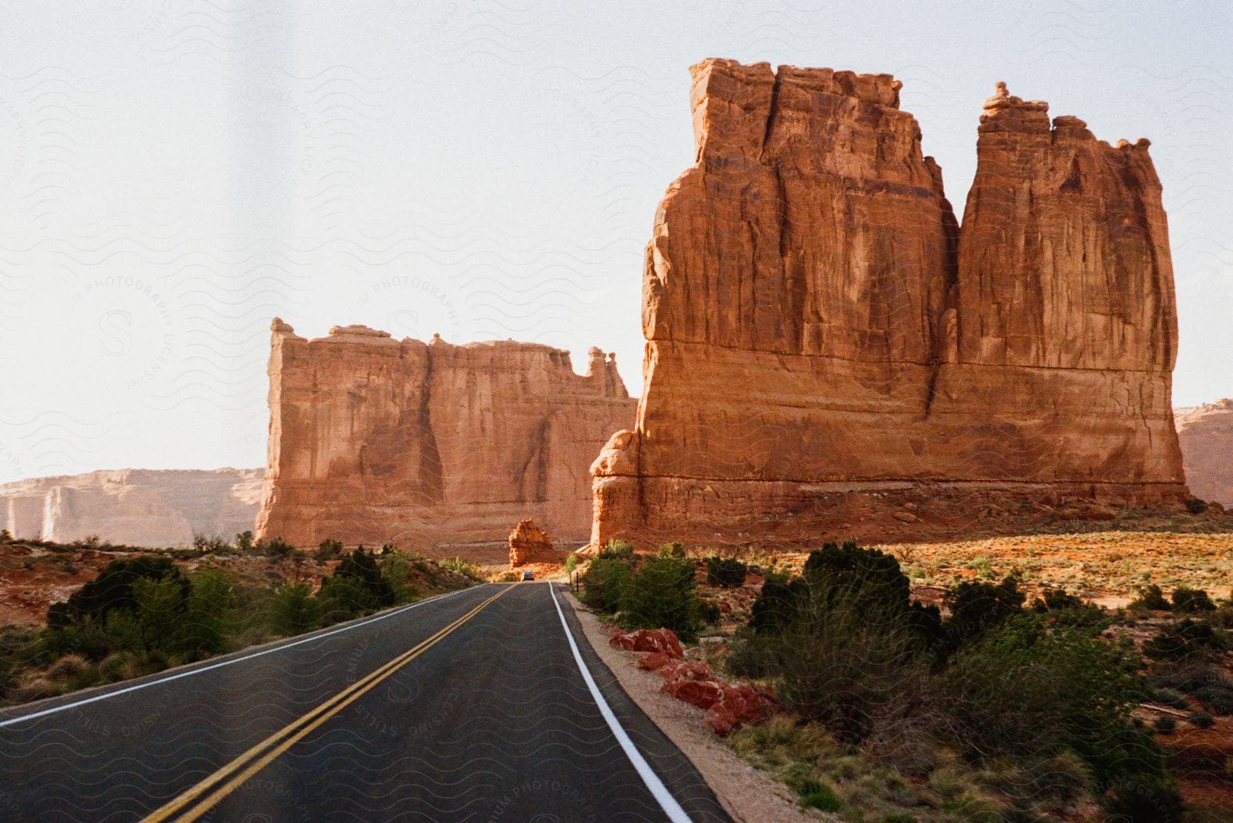 An automobile travels on a road near tall rock formations in the desert