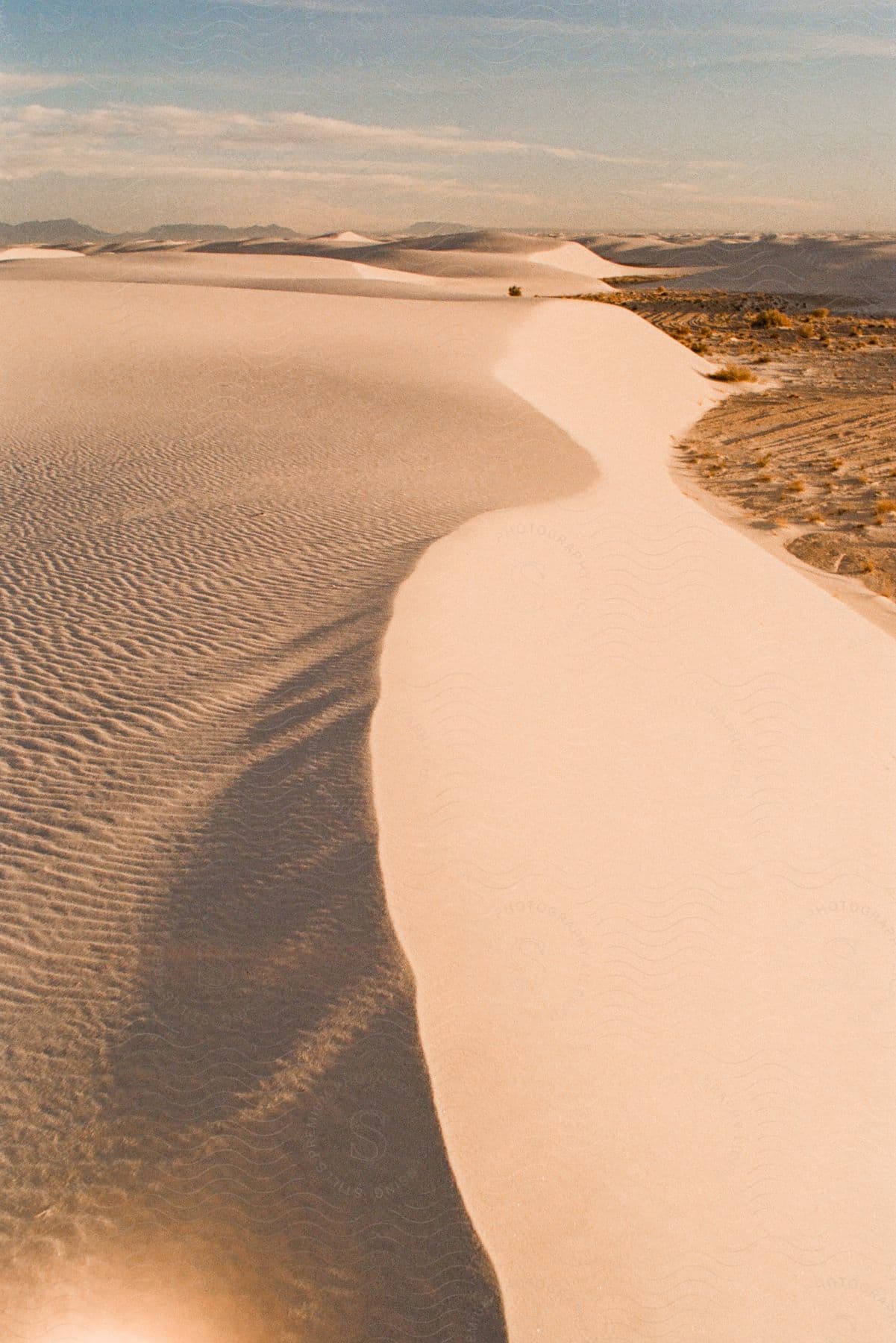 A desert with ripples in the sand and sand dunes in the distance.