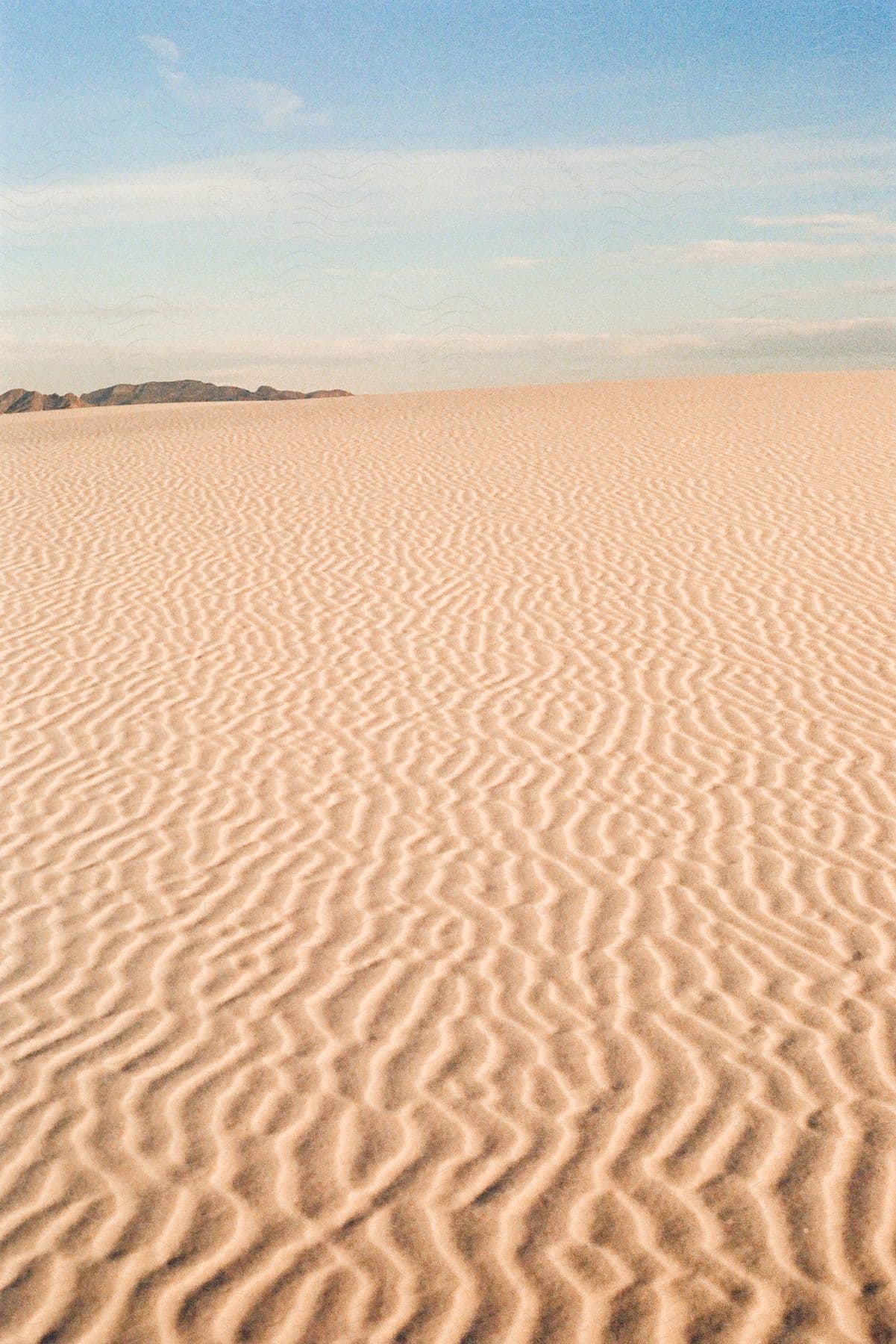 Waves in sand dunes on a sunny day with clouds in the sky.