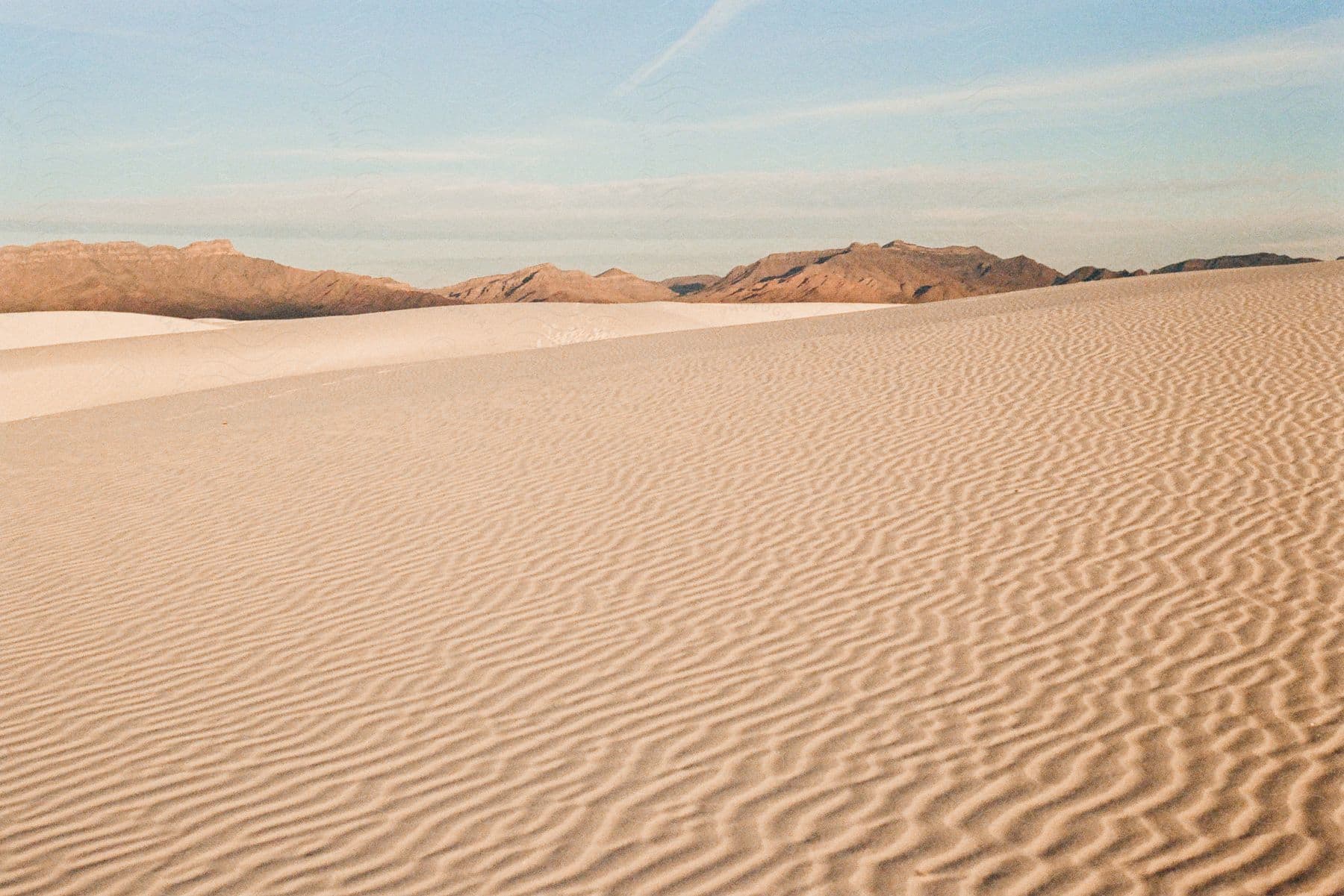 Stock photo of a desert with ripples on the sand and sand dunes in the distance.