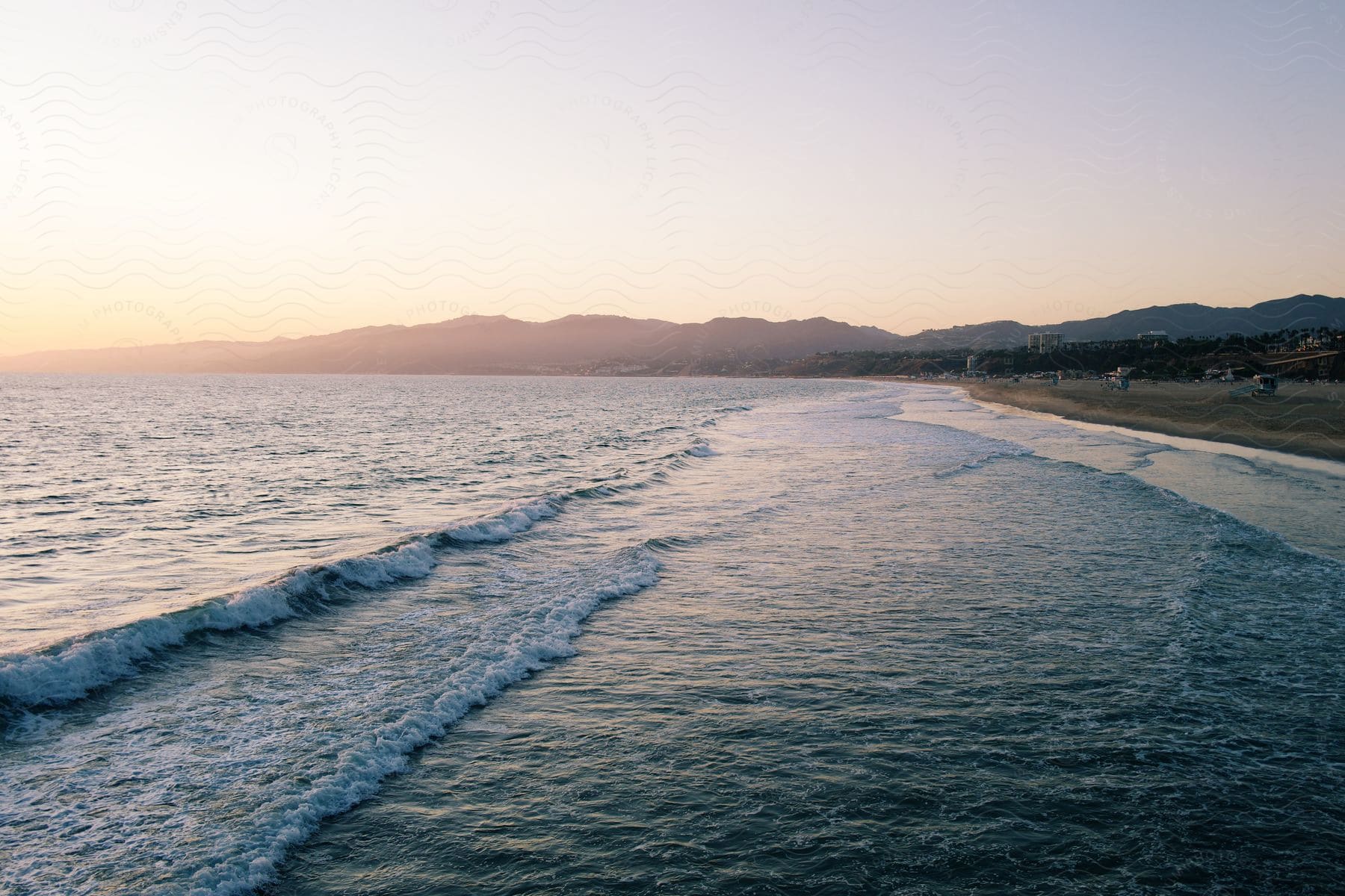 Waves roll onto beach near coastal town and mountains at sunrise.