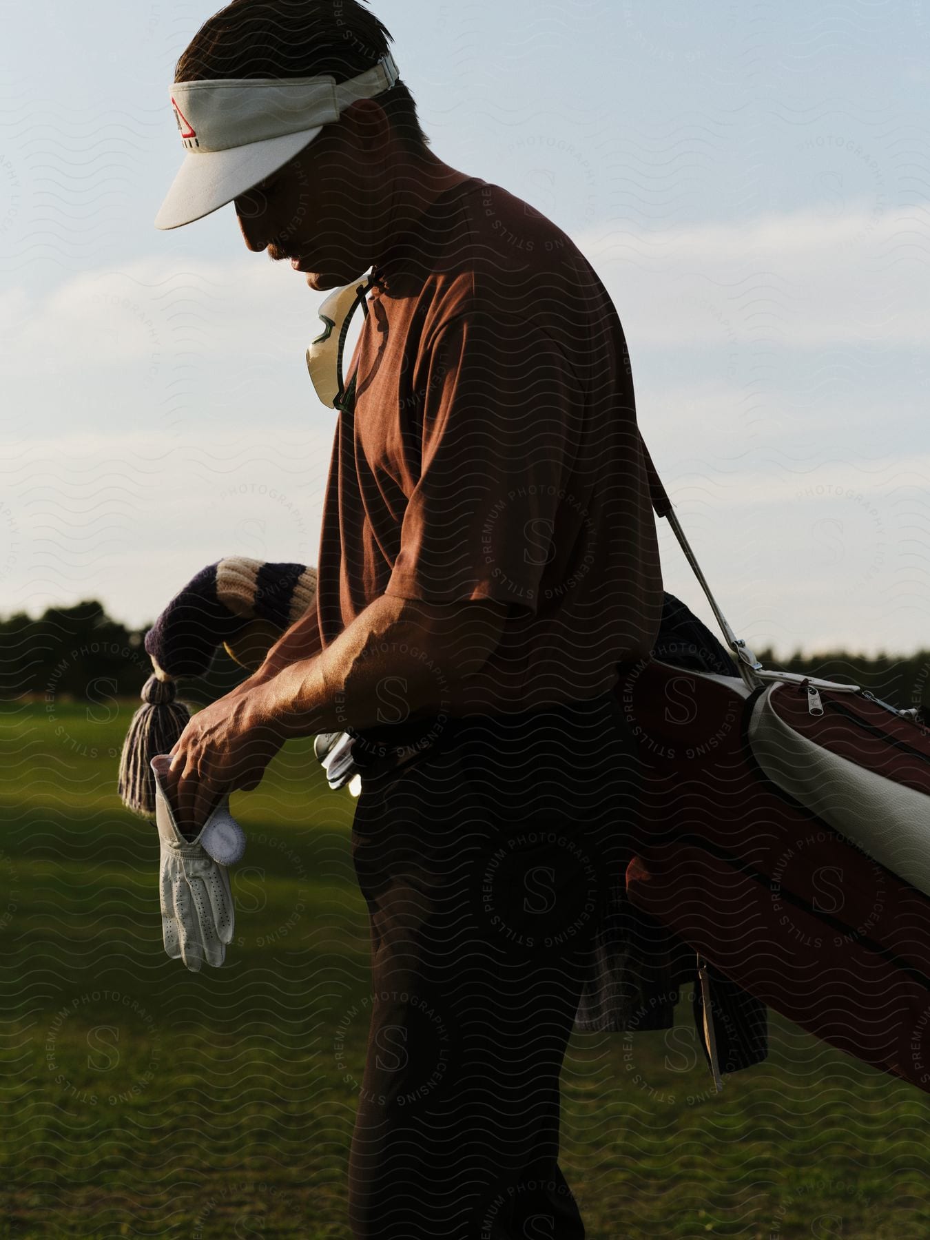 Golfer walks across golf course carrying golf bag on a cloudy day.