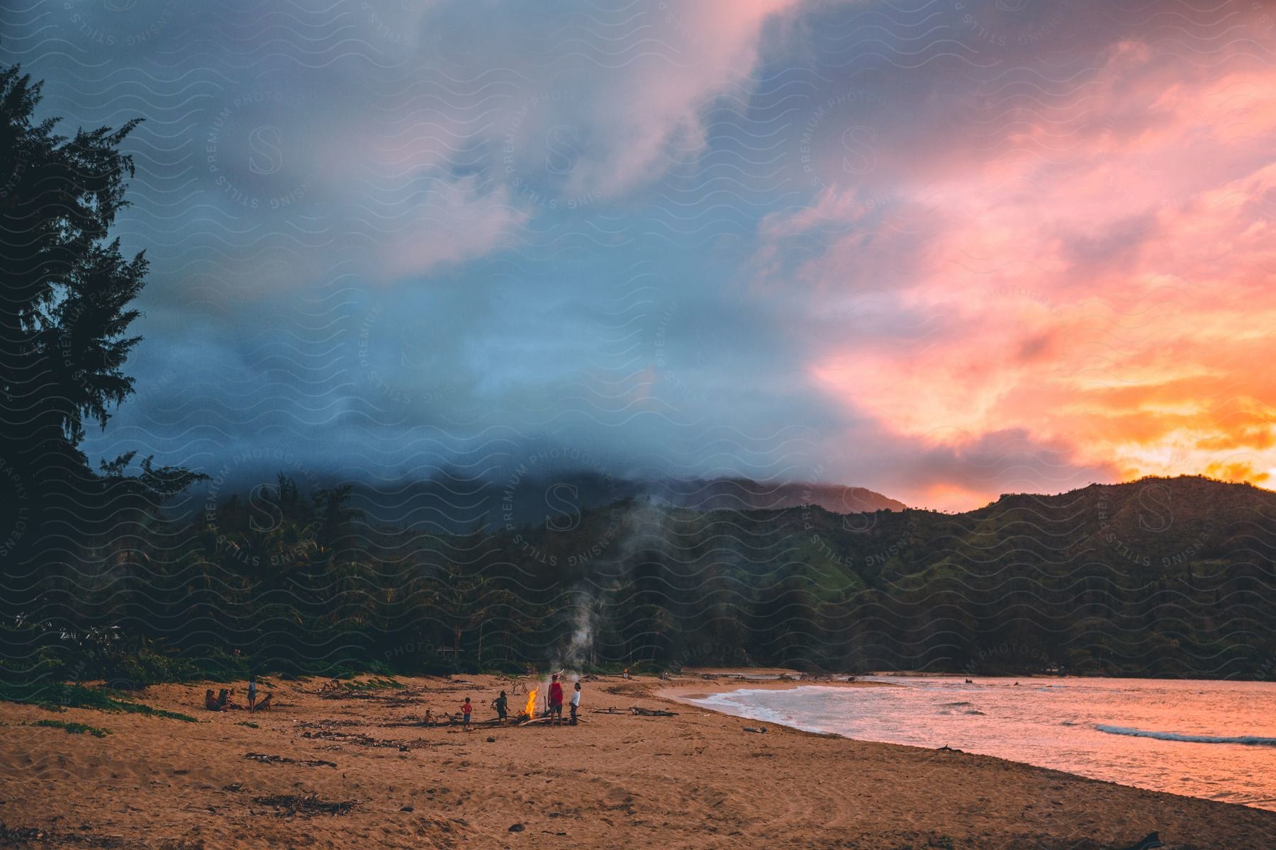 Stock photo of a family stands around a campfire on the beach