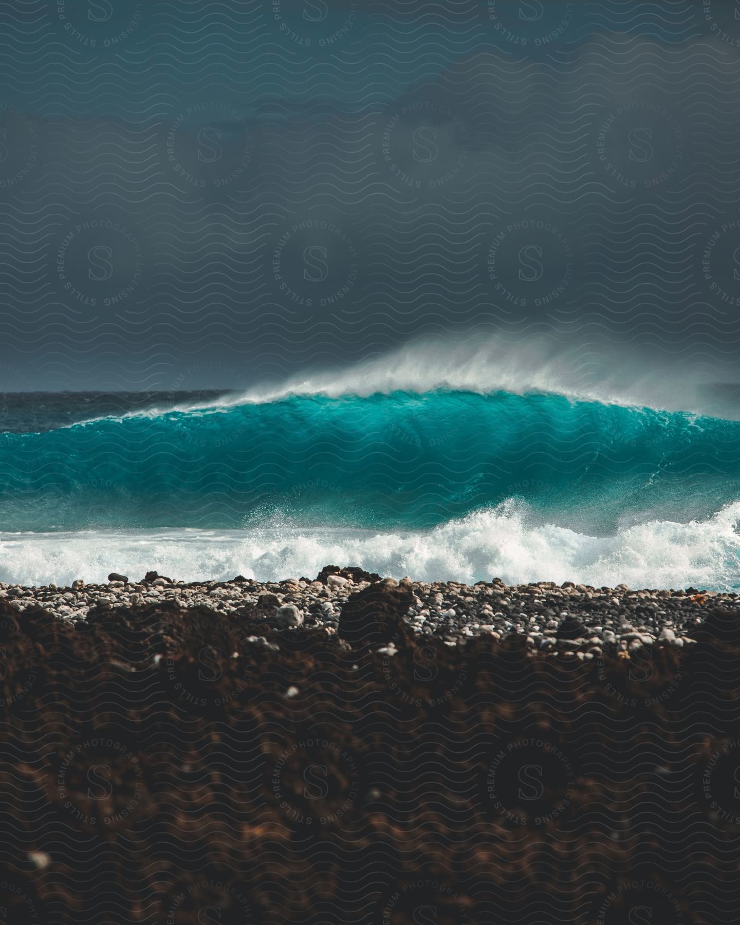 A clear blue wave splashes as it rolls into shore under a dark cloudy sky