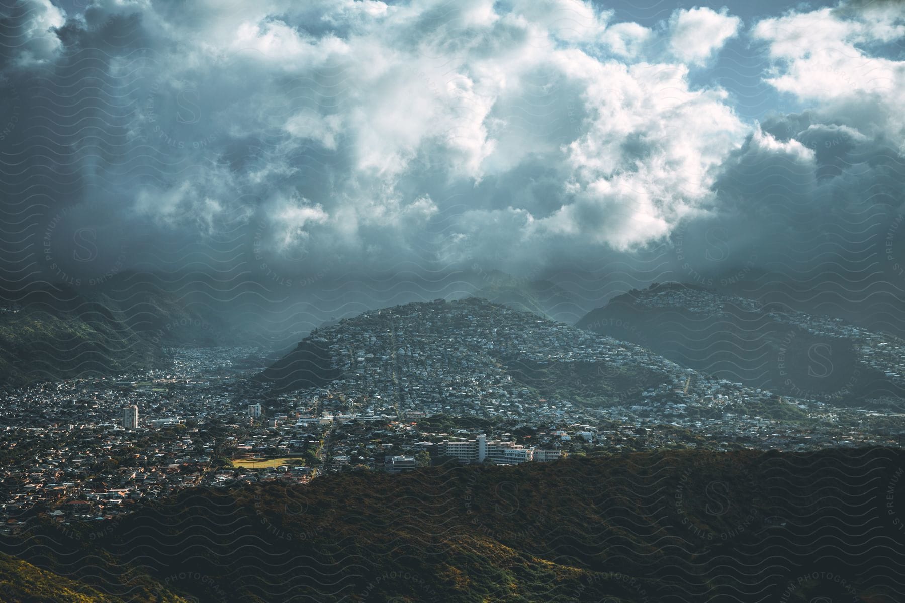 A city nestled between a mountain and storm clouds, bathed in golden sunlight, is visible from Diamond Head State Monument.