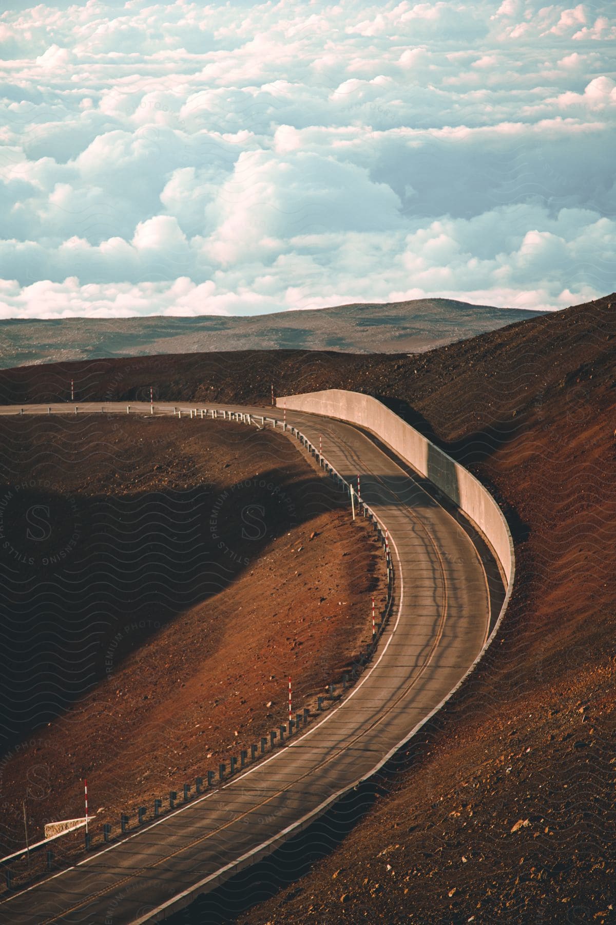 A curved, empty road winds its way through a mountain range, under a cloudy sky.