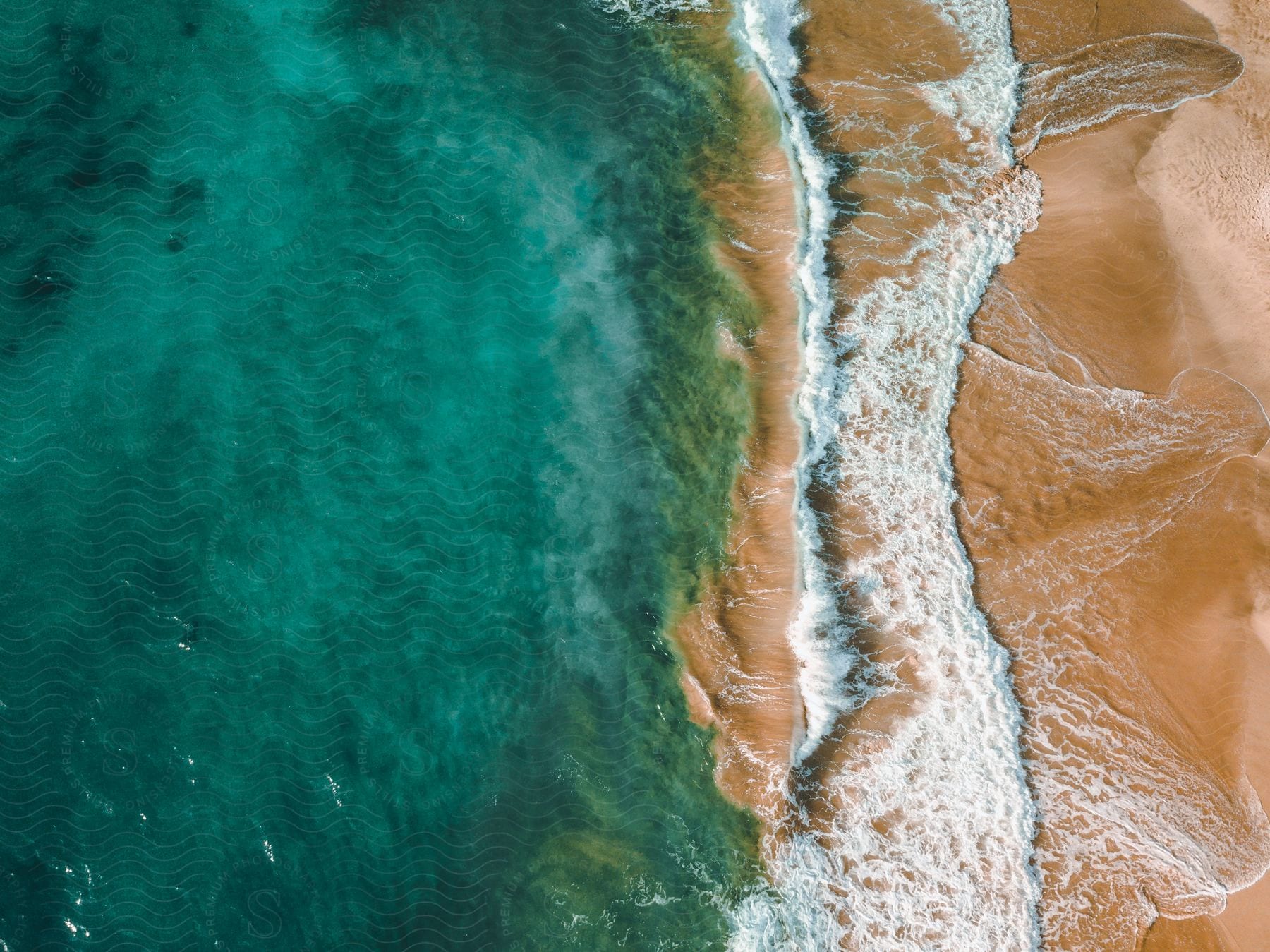 An aerial view pointing straight down of waves crashing on the beach.