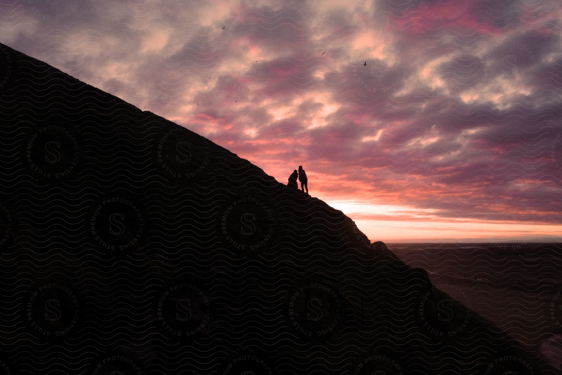 Silhouette of two people on a mountain during the evening sunset.