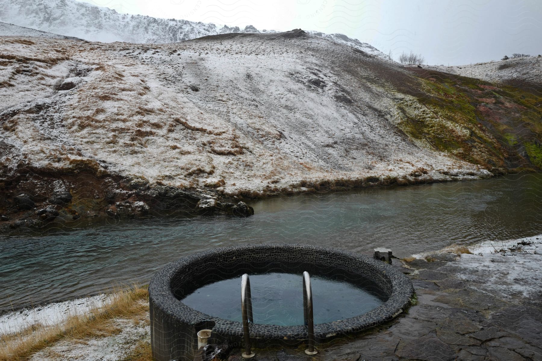 A river at the base of a hill with a hot tub along the bank