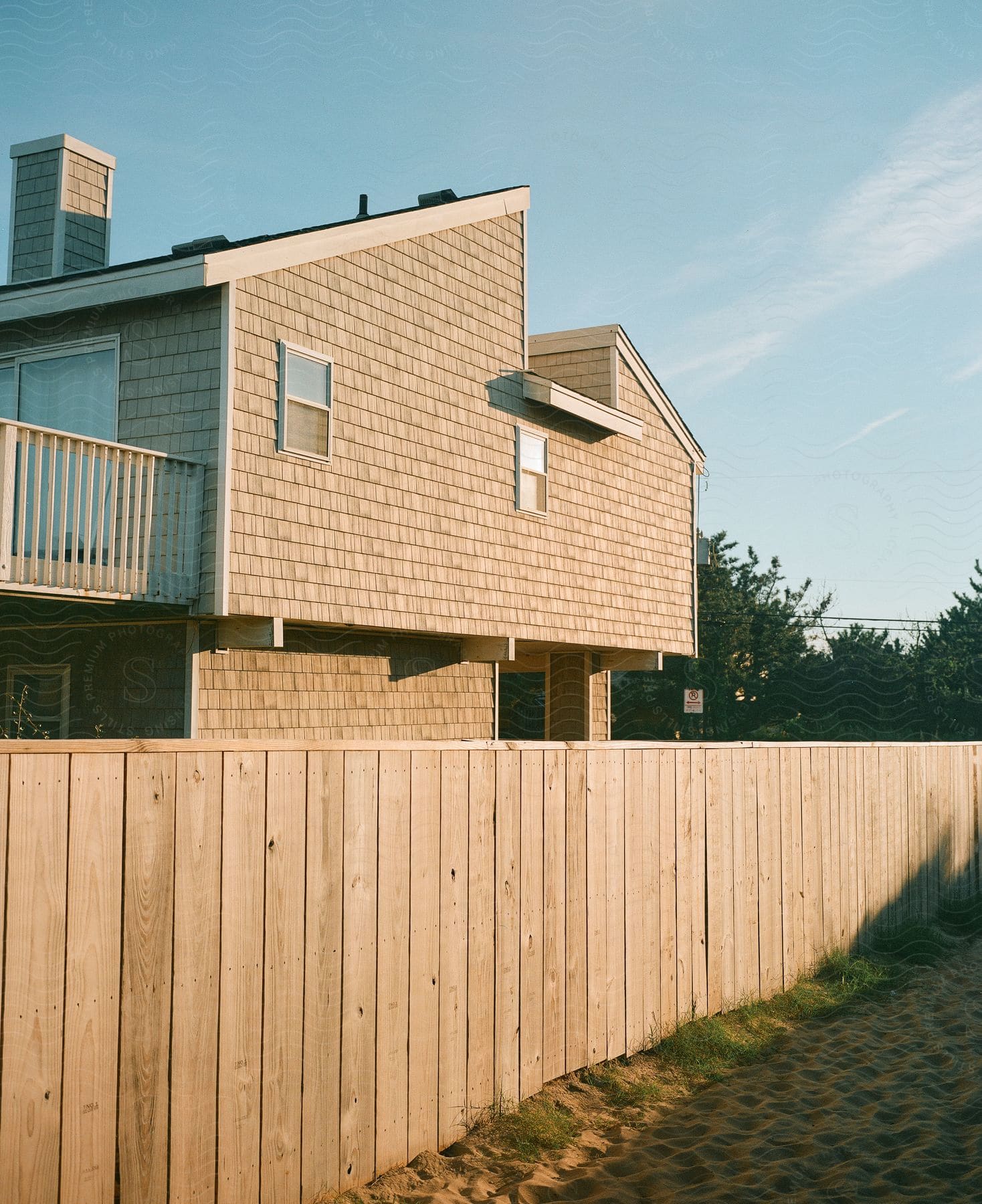 A beach house with a wooden fence and a sandy path leading to the beach, marked by footprints.