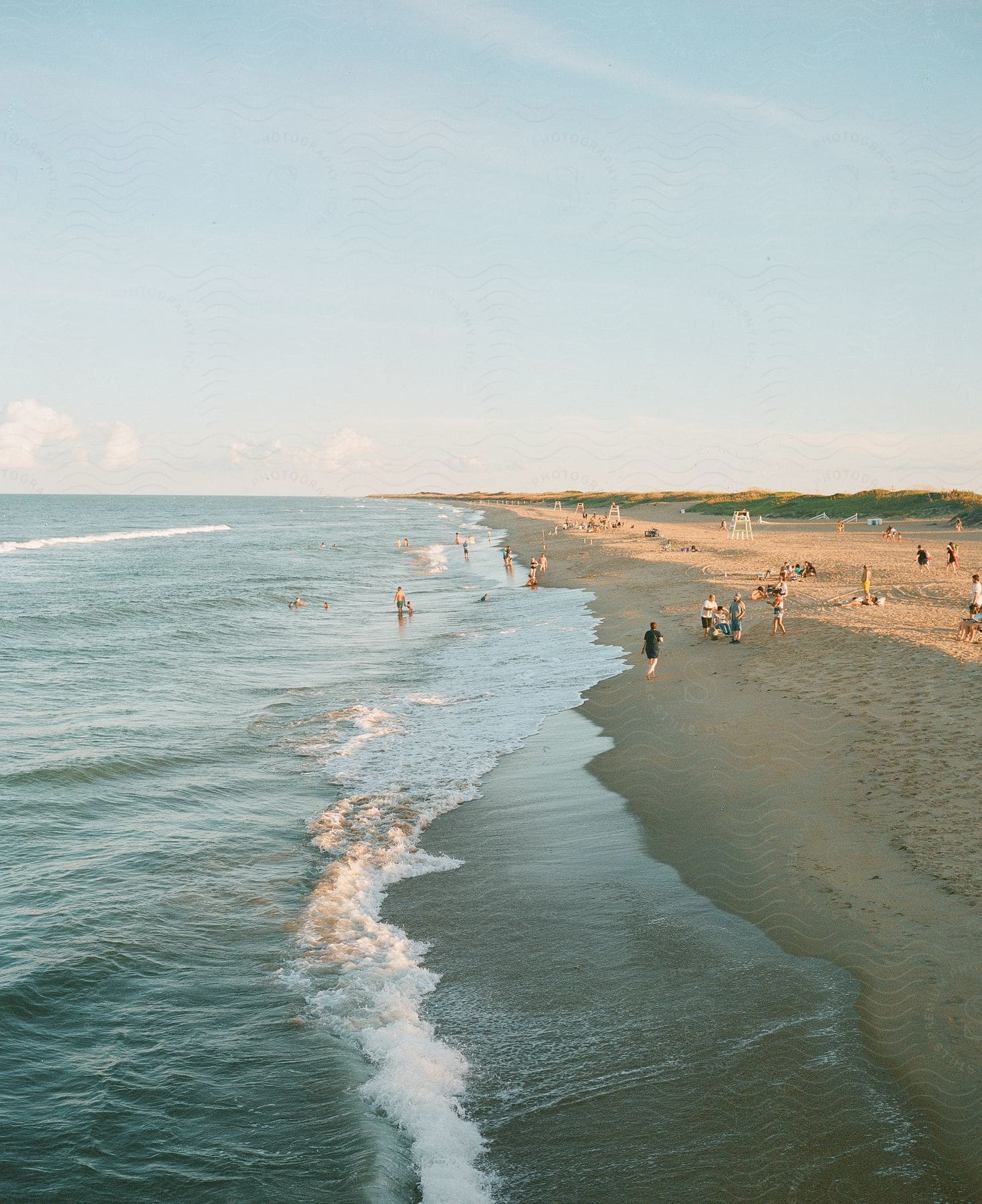 A busy beach on a sunny day, with people swimming, sunbathing, and walking along the shore.