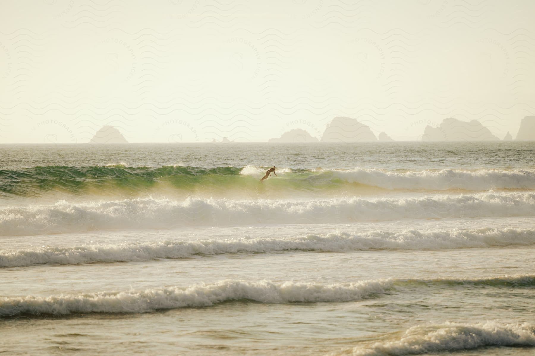 A surfer rides a wave in the ocean, surrounded by crashing waves and mountains in the distance.