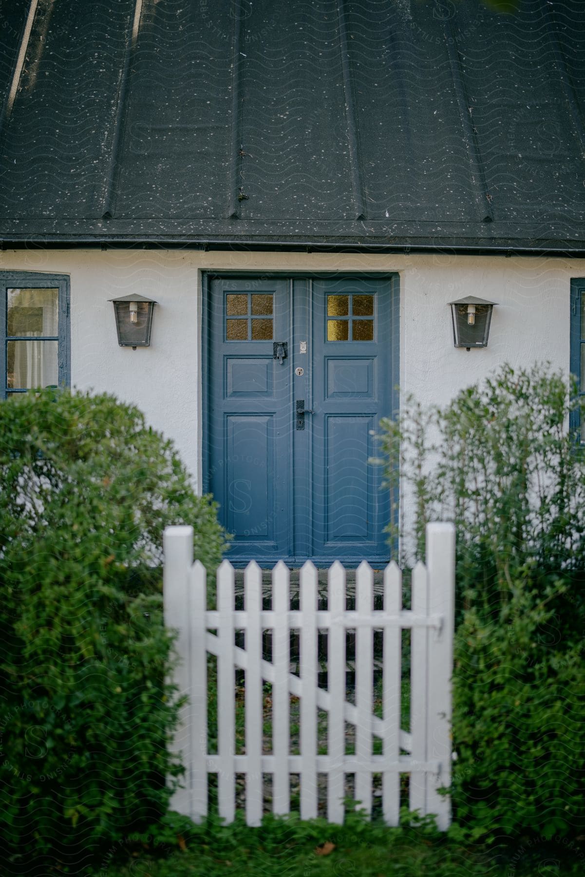 A farm house with a blue double door and a picket fence gate.