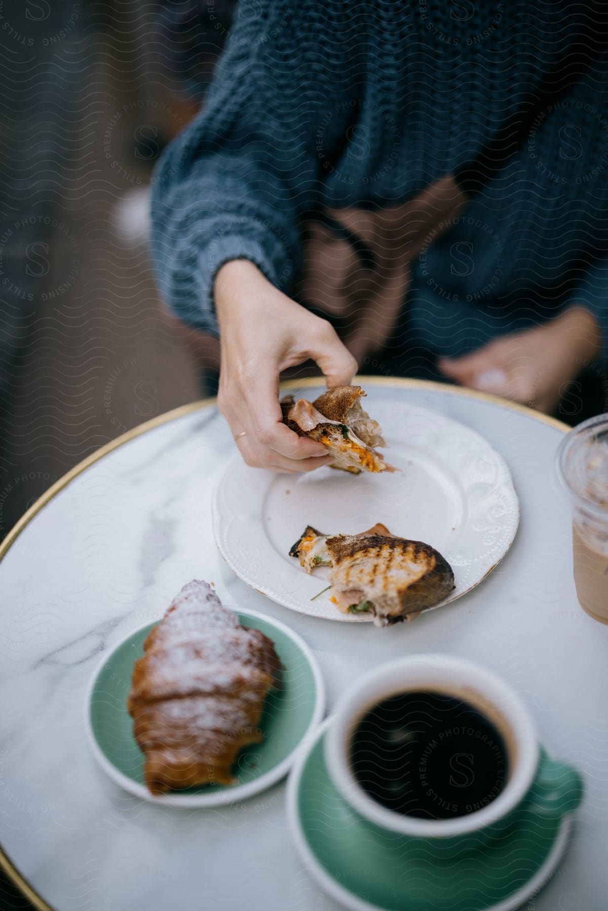 A woman eating a sandwich sitting at a table outdoors at a cafe