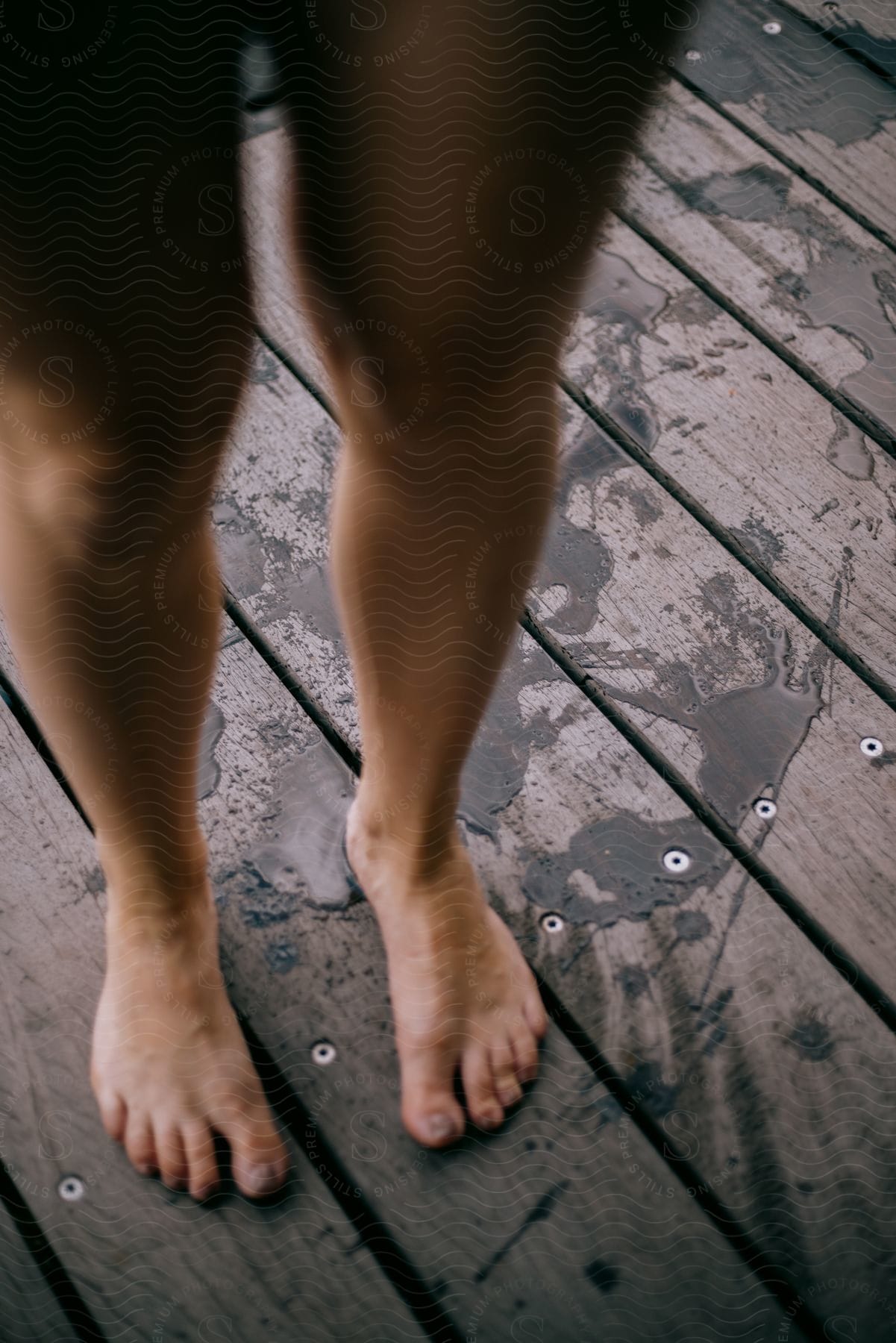 A girl is standing on a wooden deck with no shoes on.