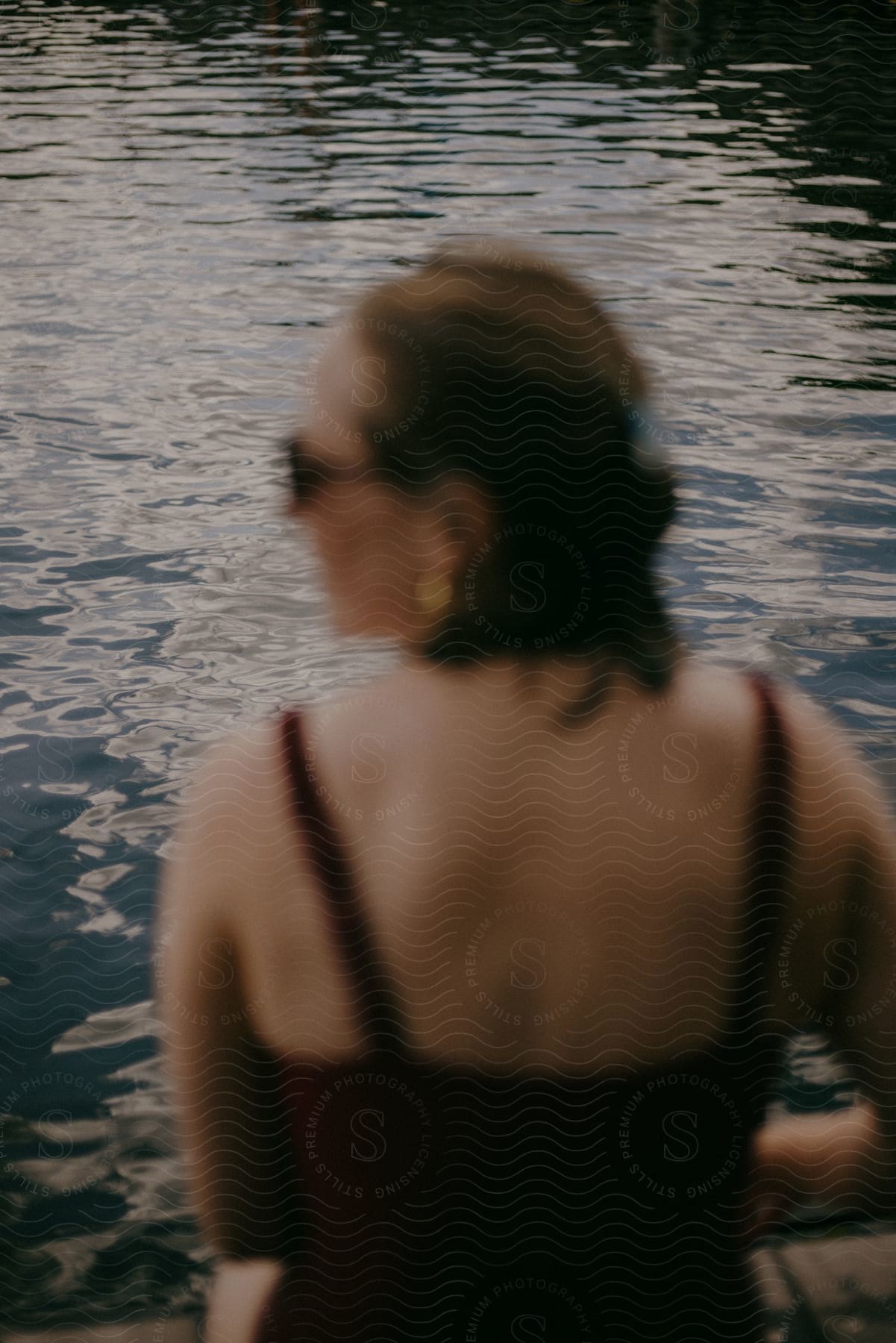 woman in a red bikini is seen sitting on the edge of a pool, her figure blurred