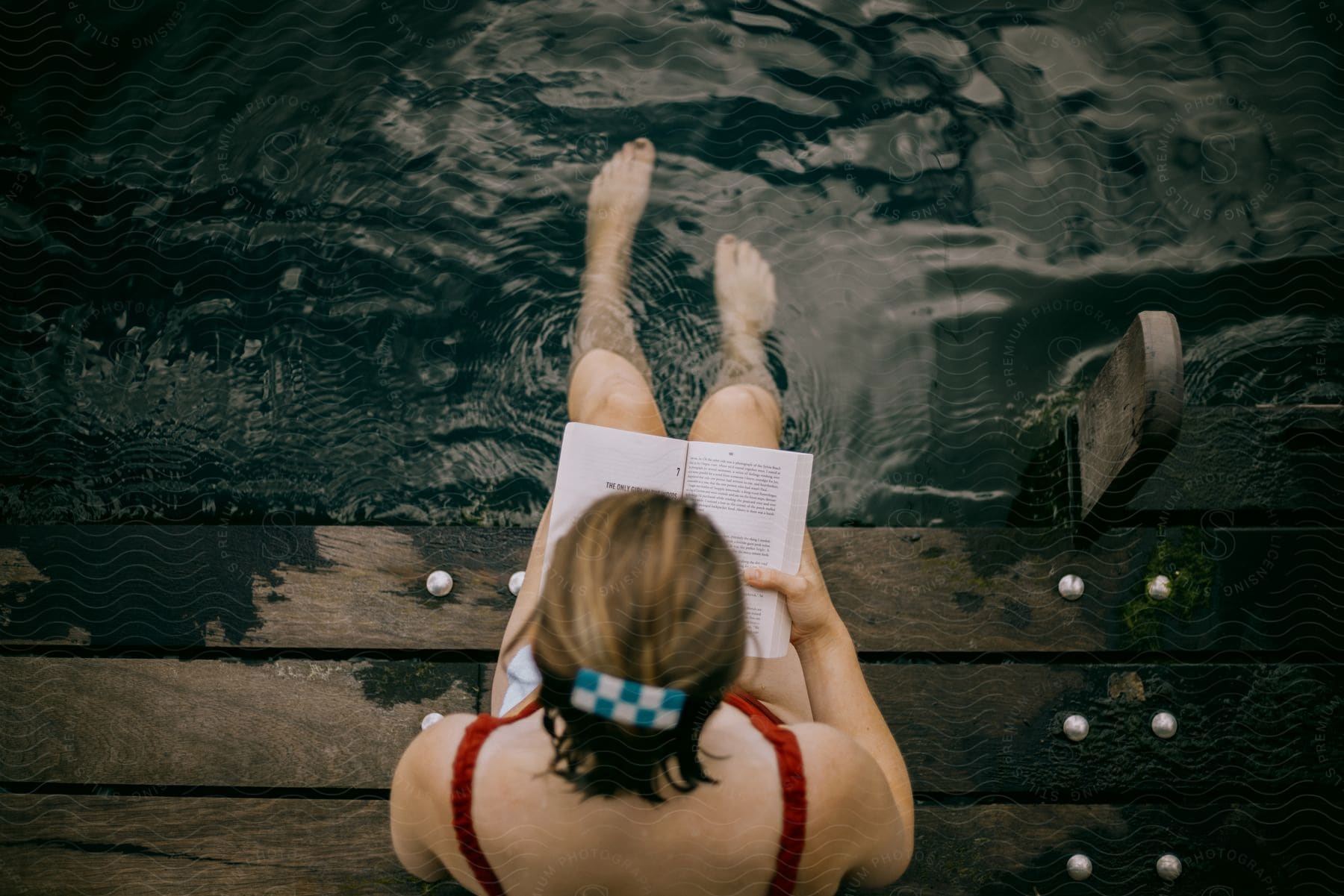 A woman sitting outside reading a book while soaking her feet in water