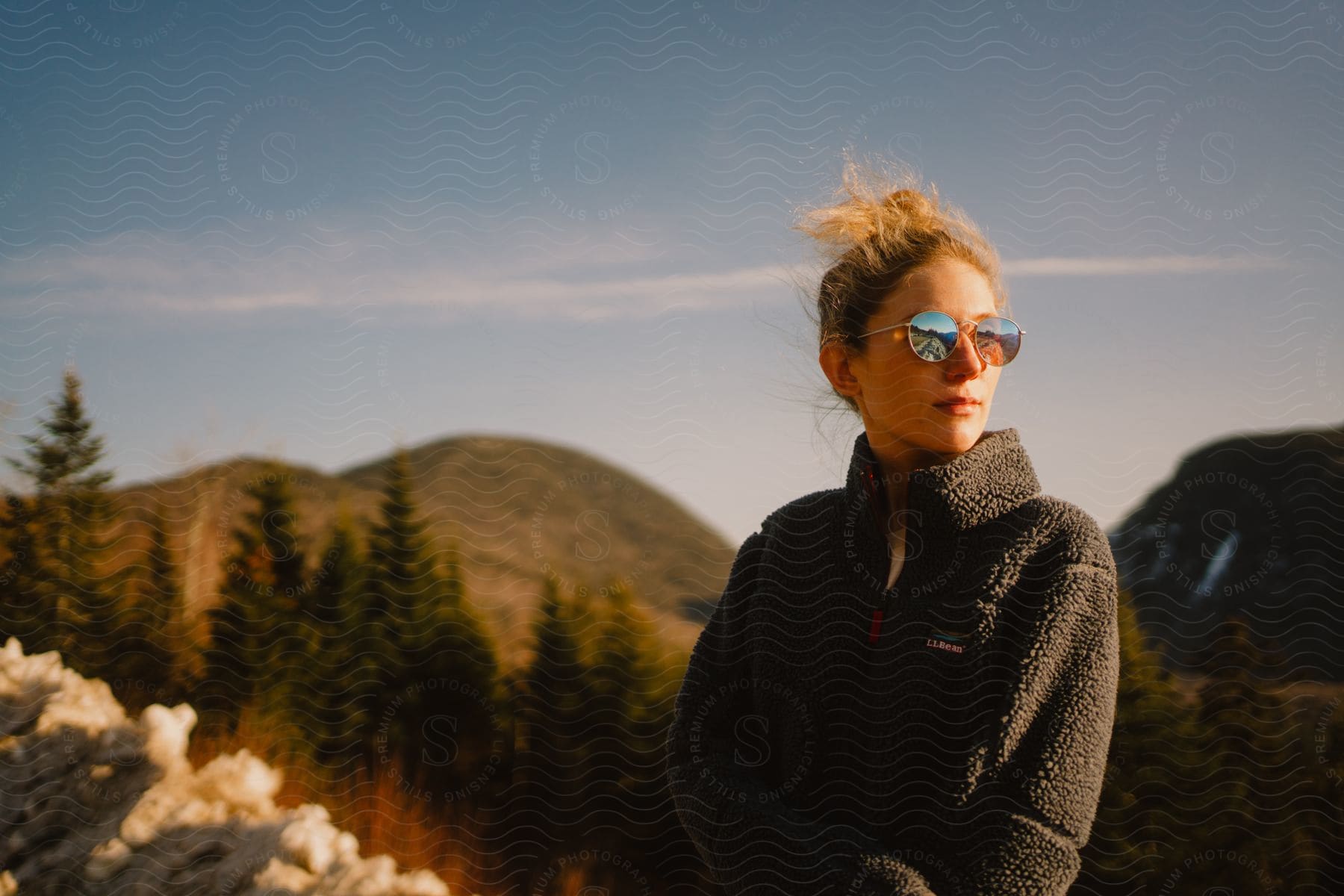 Portrait of a blonde woman with glasses in a natural environment with trees and mountains.