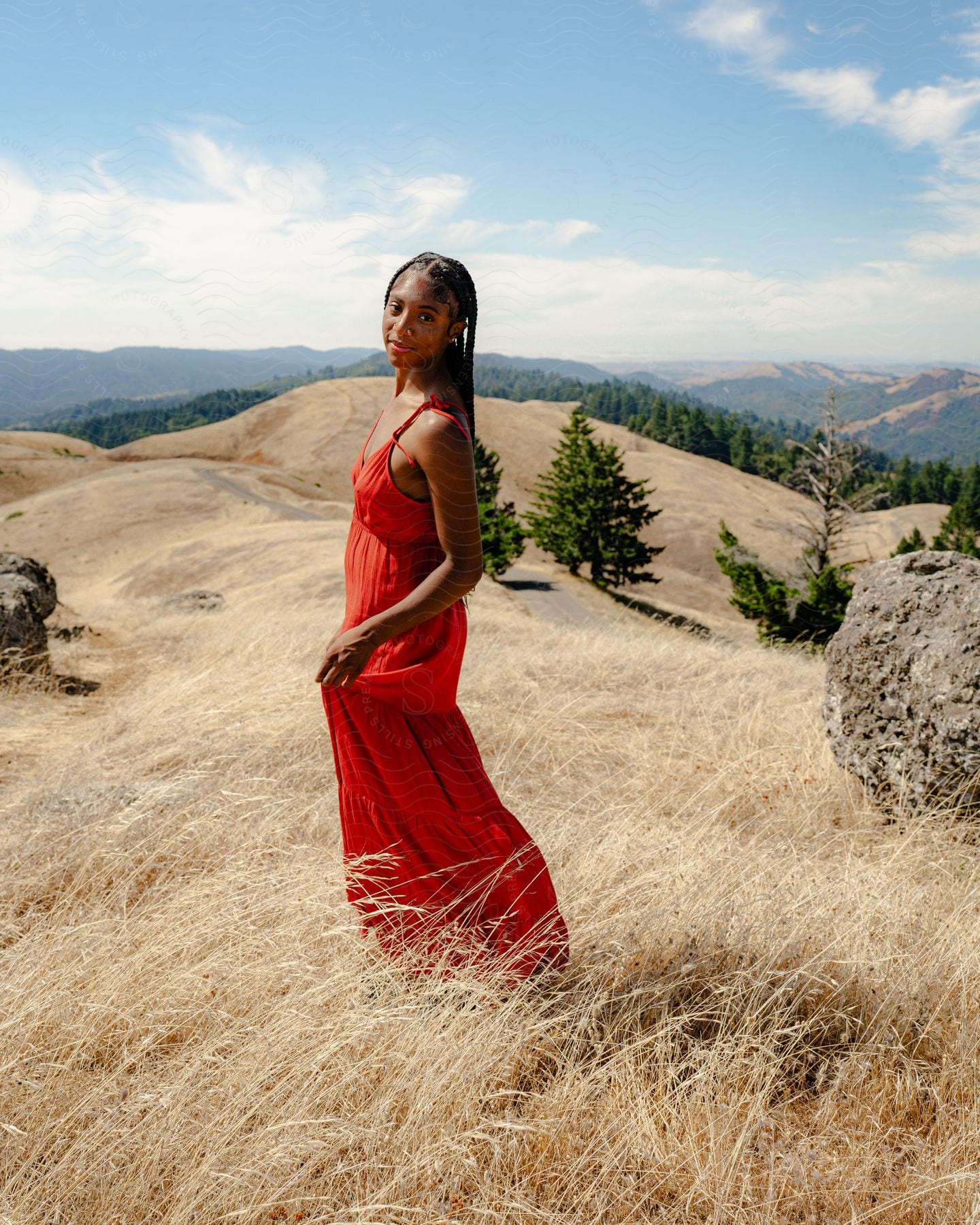 A woman standing in a dried grass field while wearing a bright red dress.