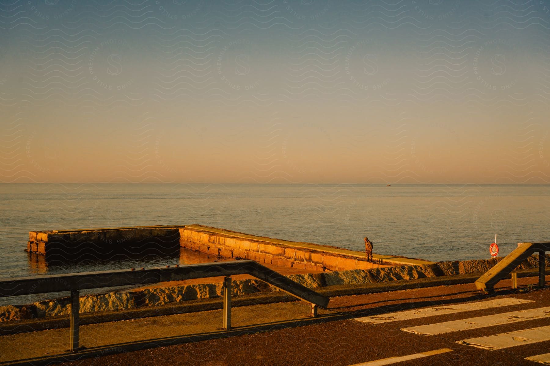 Unrecognizable person on a pier, observing the ocean during sunrise.