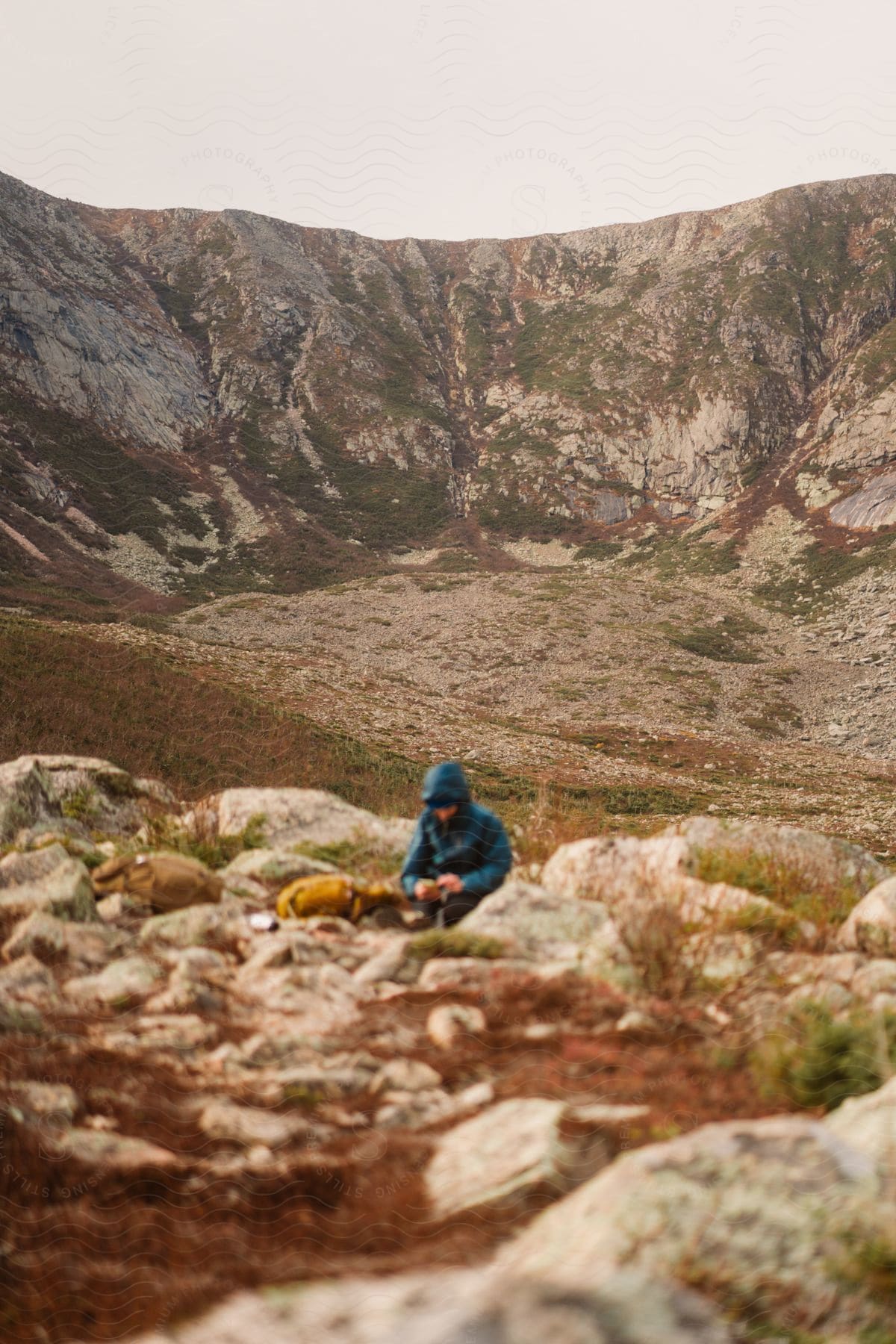 A man crouches in a field of rocks on a mountainside.