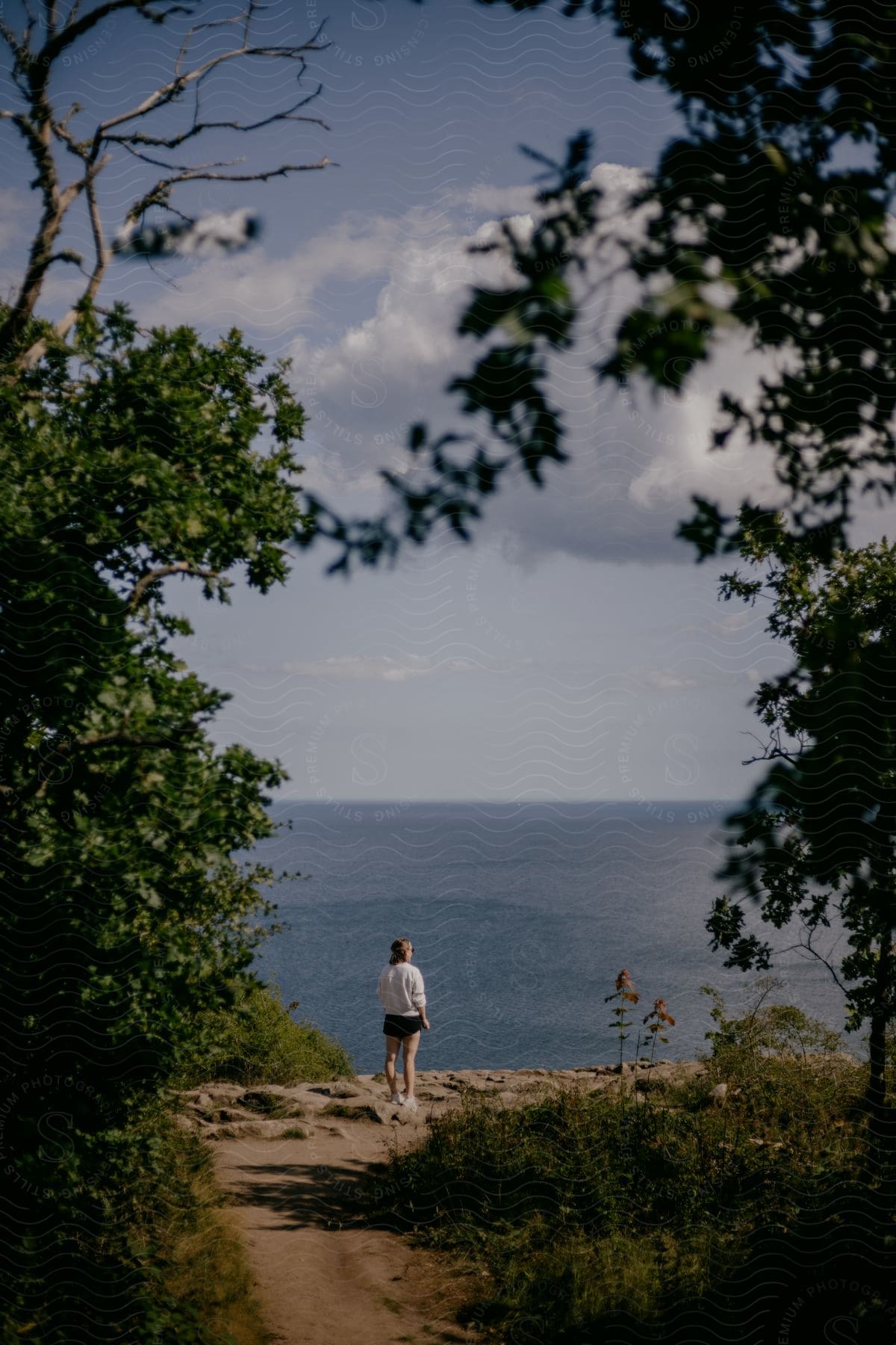 Woman stands on coastal trail and looks out toward ocean.