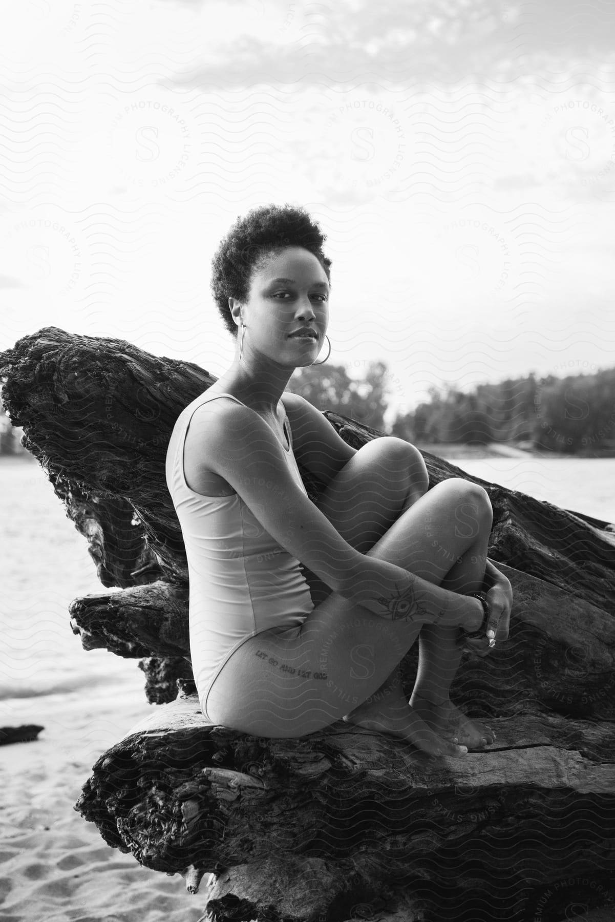 Woman sits on large piece of driftwood on beach in swimsuit.