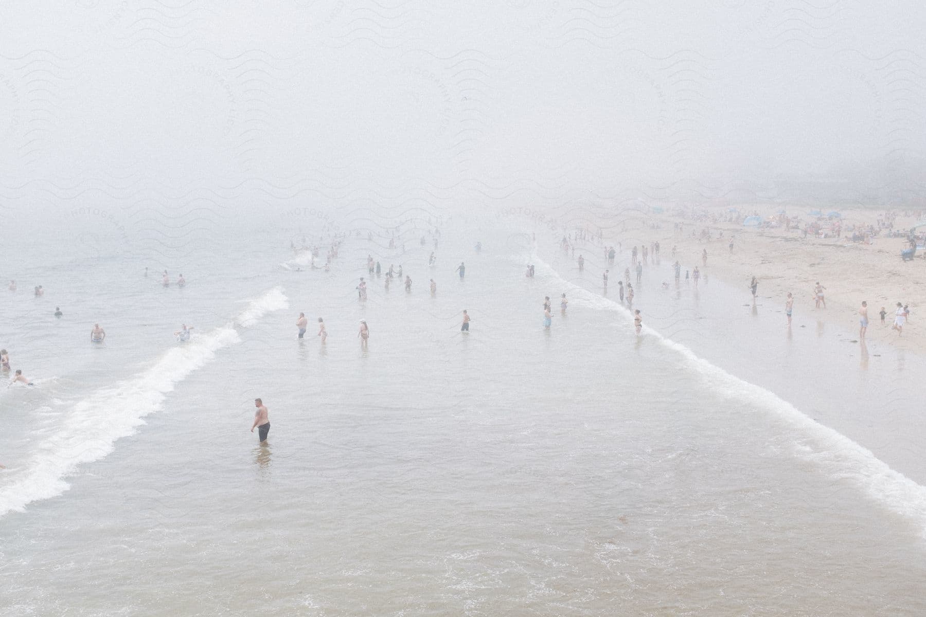 Beachgoers enjoy the ocean on a very foggy day.