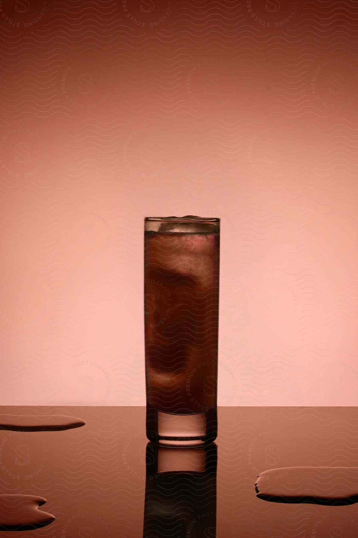 A glass of beverage with ice stands on the counter with some liquid drops.