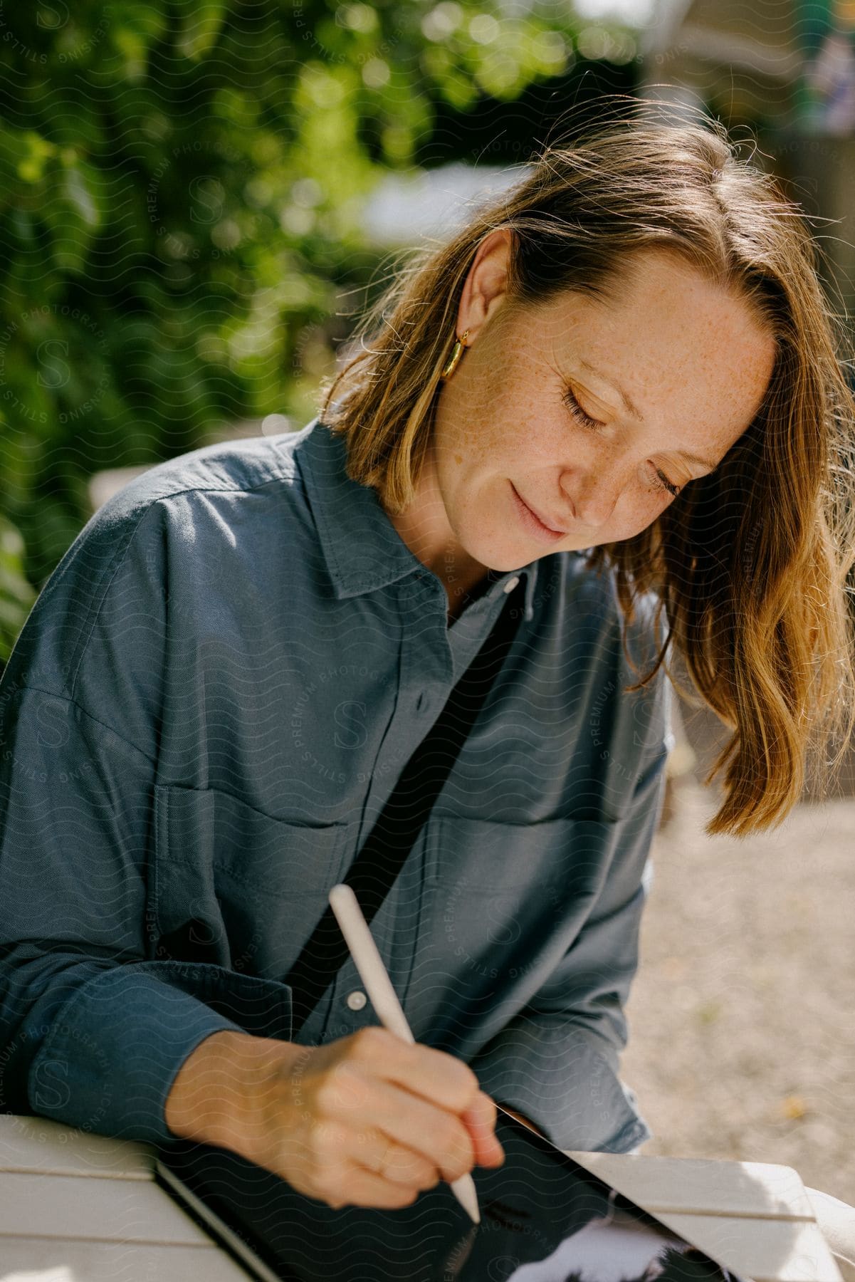 Stock photo of a woman is sitting at a table outside writing on a tablet computer with a stylus