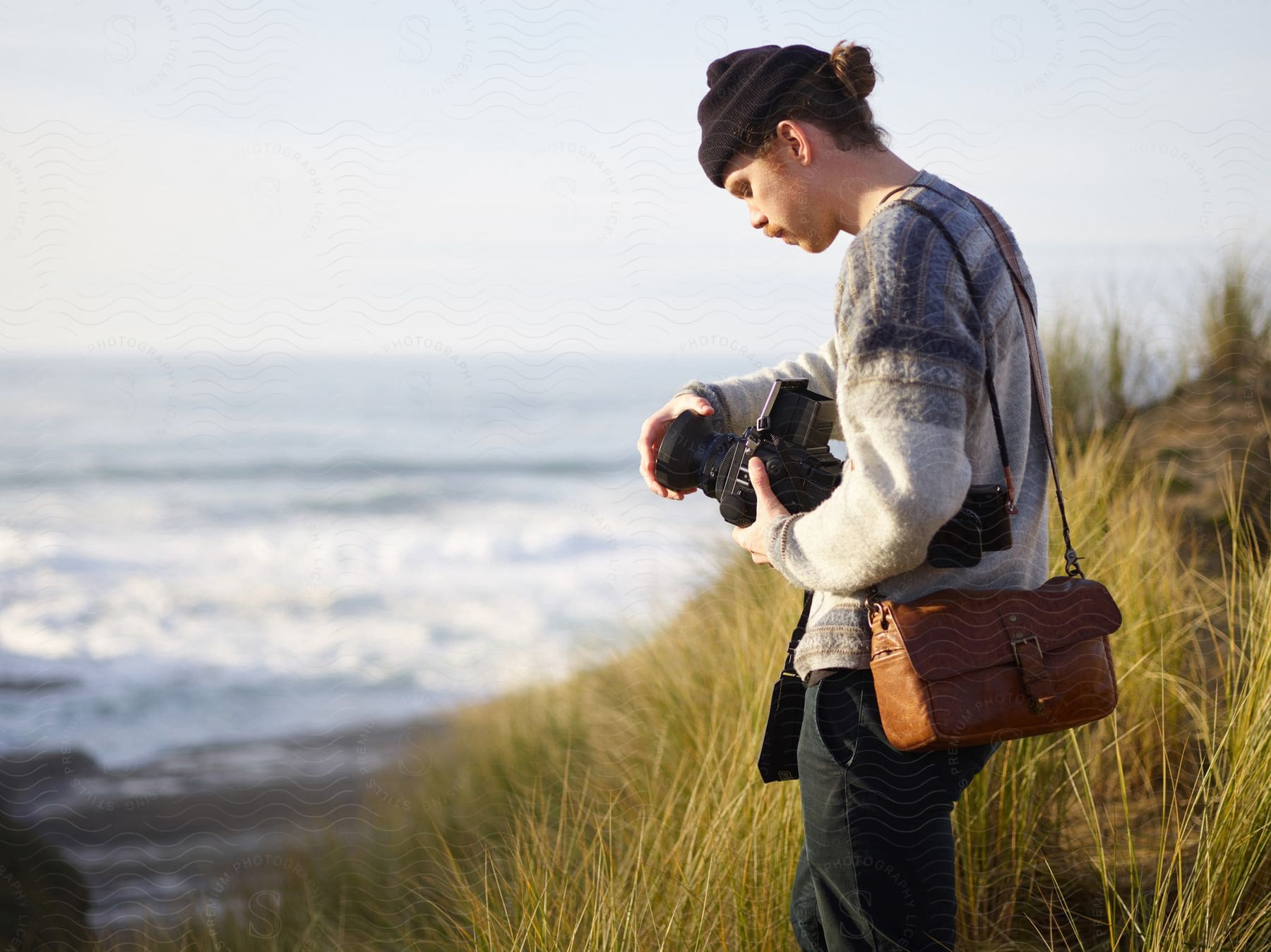 Stock photo of photographer standing by the sea, setting up their camera.