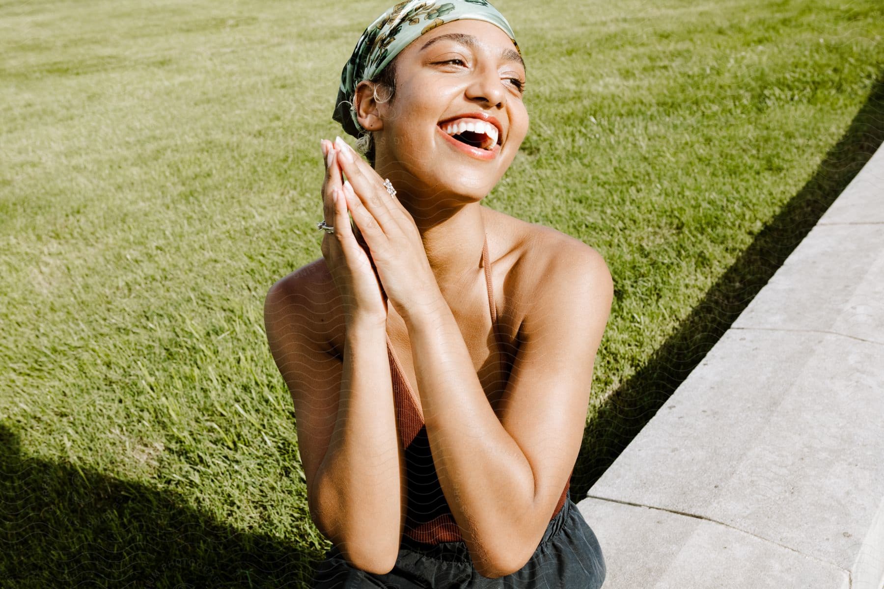 A woman is sitting on a cement wall smiling and staring into the distance.