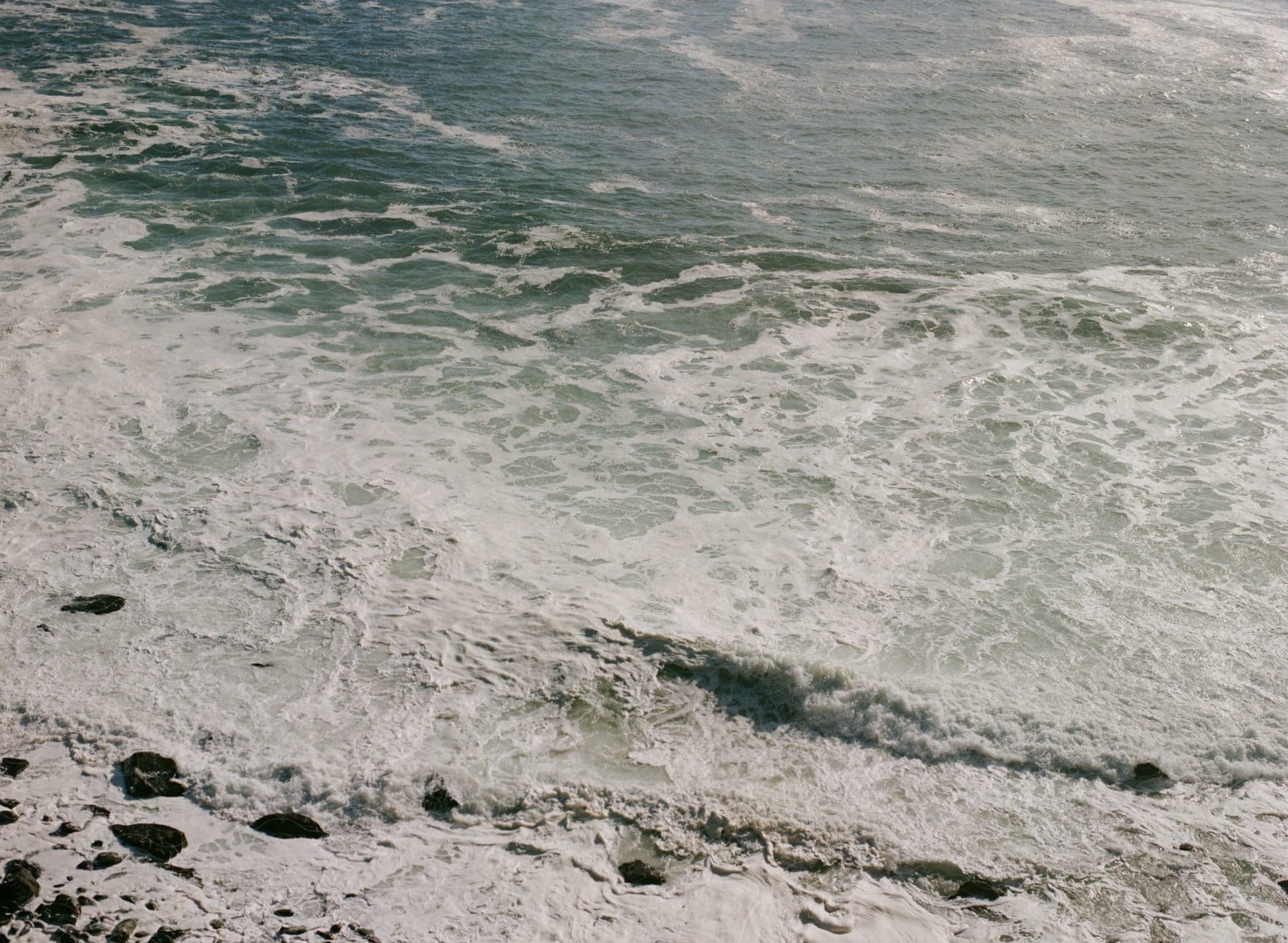 Whitewash waves crash onto a rocky shore on a sunny day.