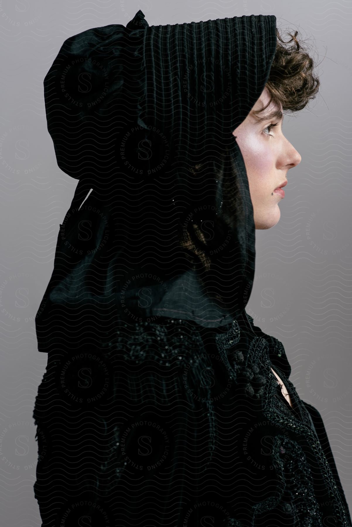 A woman wearing a black sweater and black bonnet is turned to her side