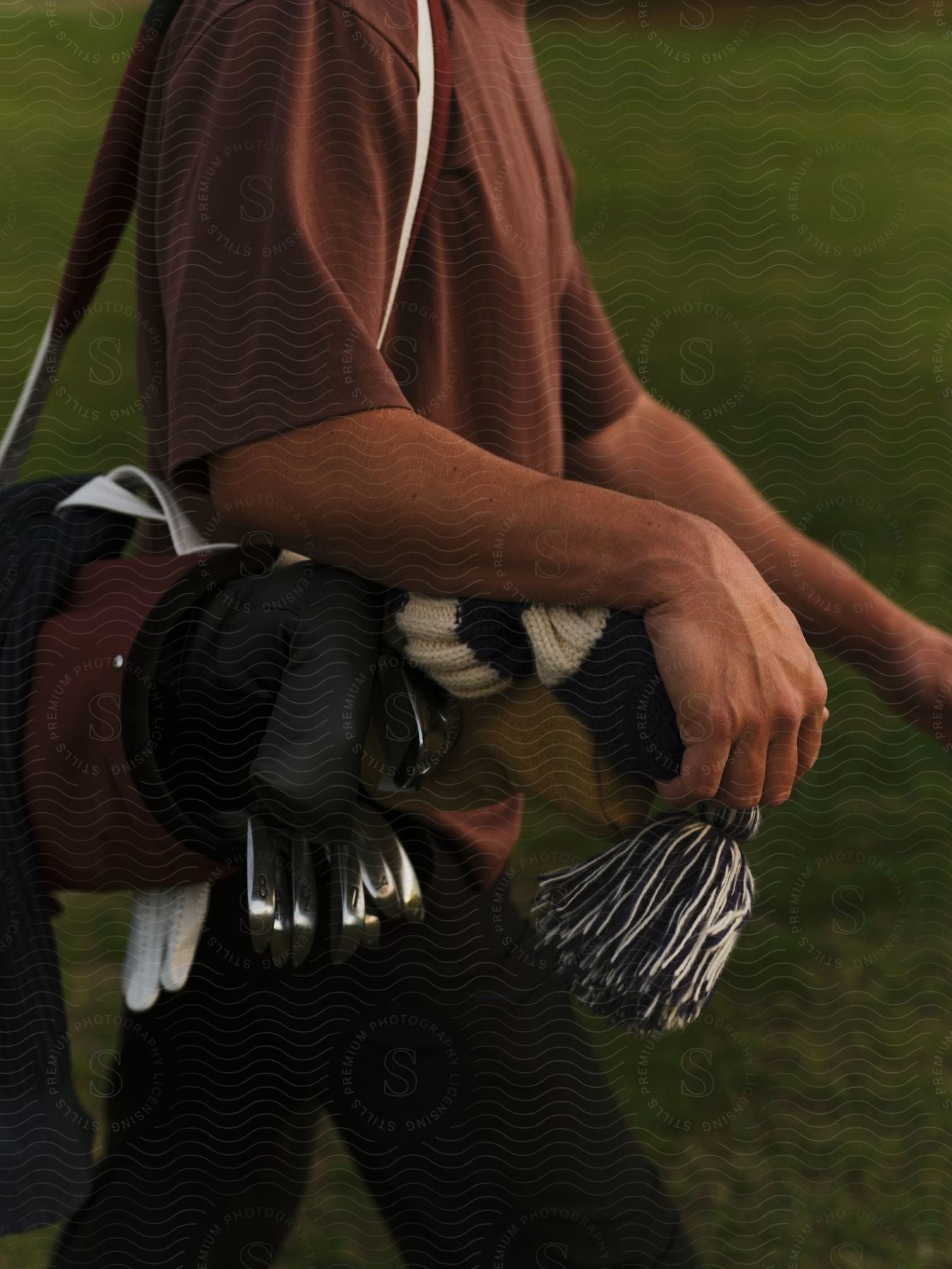 The torso of a golfer carrying a golf bag over one shoulder walking on the green