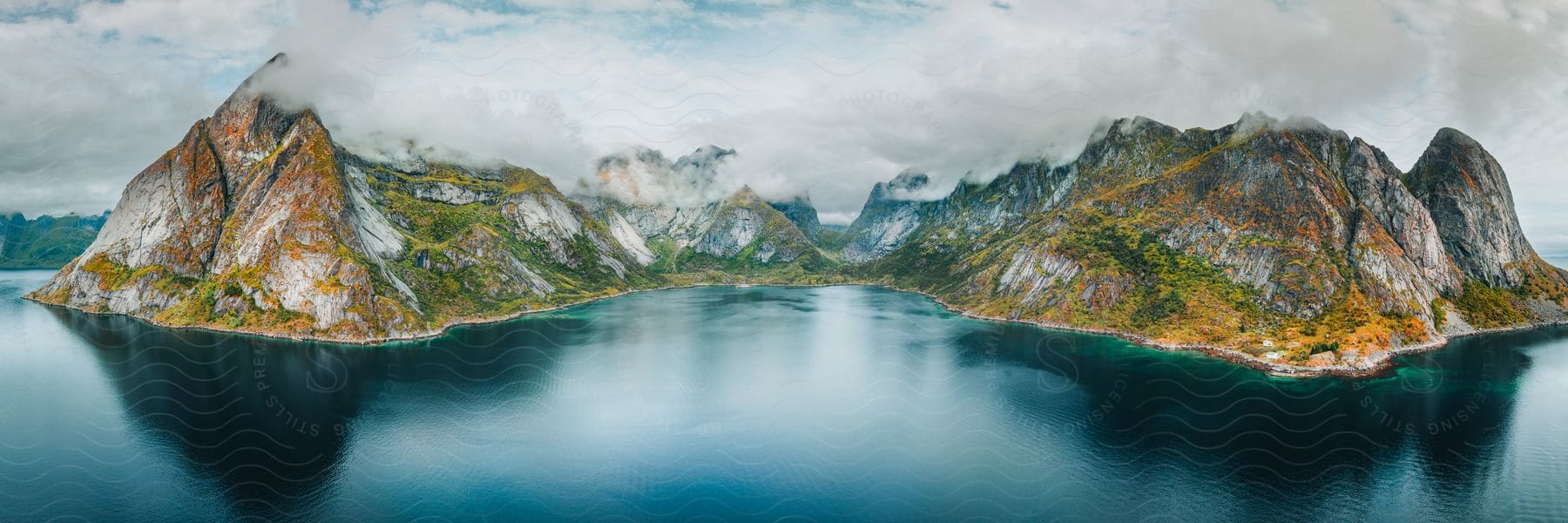 Dark Blue Water Surrounding A Couple Mountains On A Cloudy Day