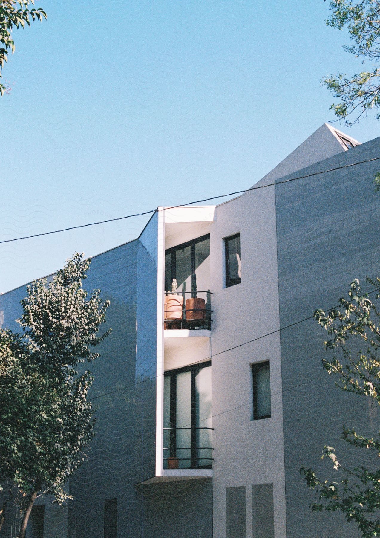 side of a modern style apartment building next to trees with the sky in the background during day time