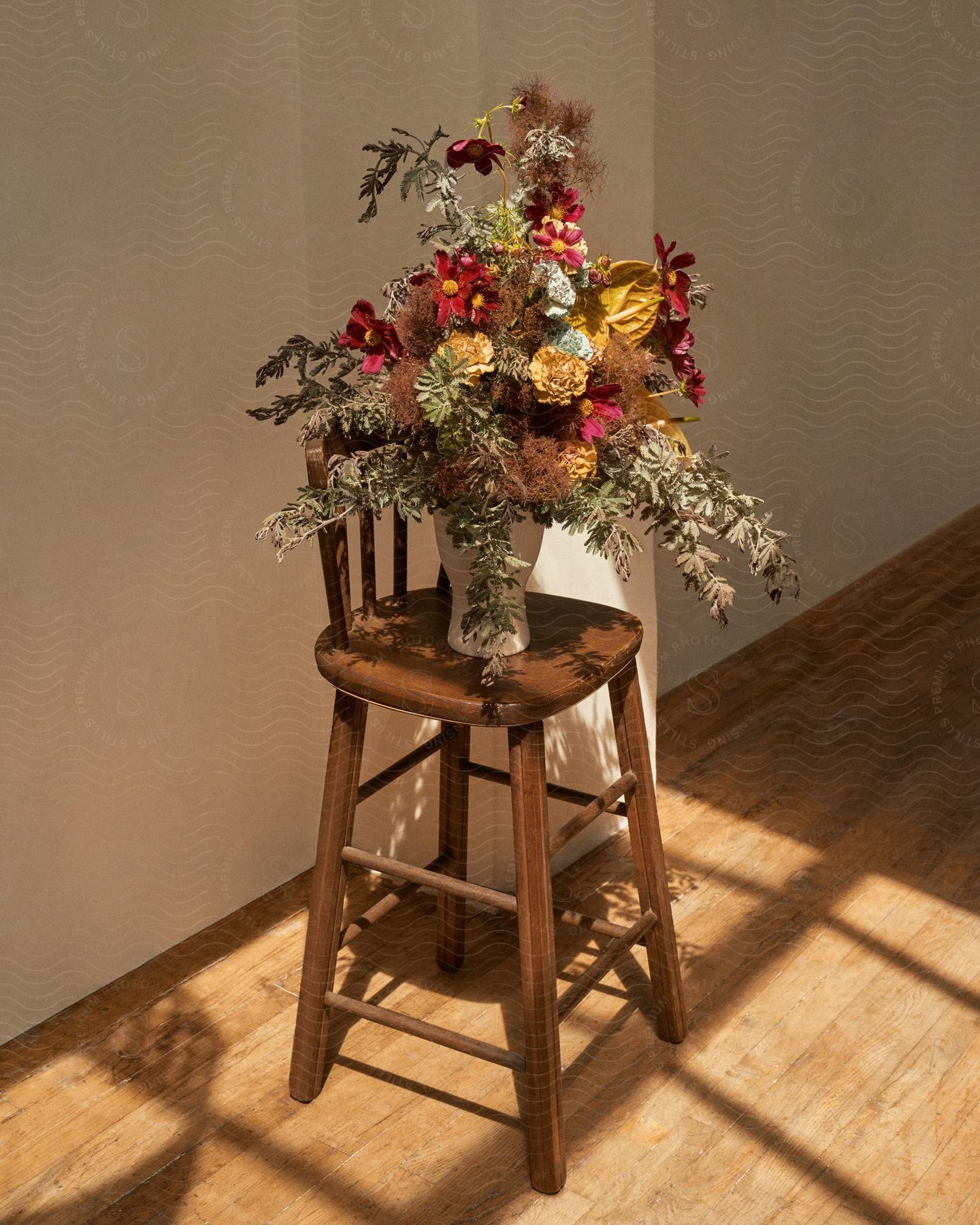 A bouquet of flowers in a glass vase is sitting on a stool near a wall