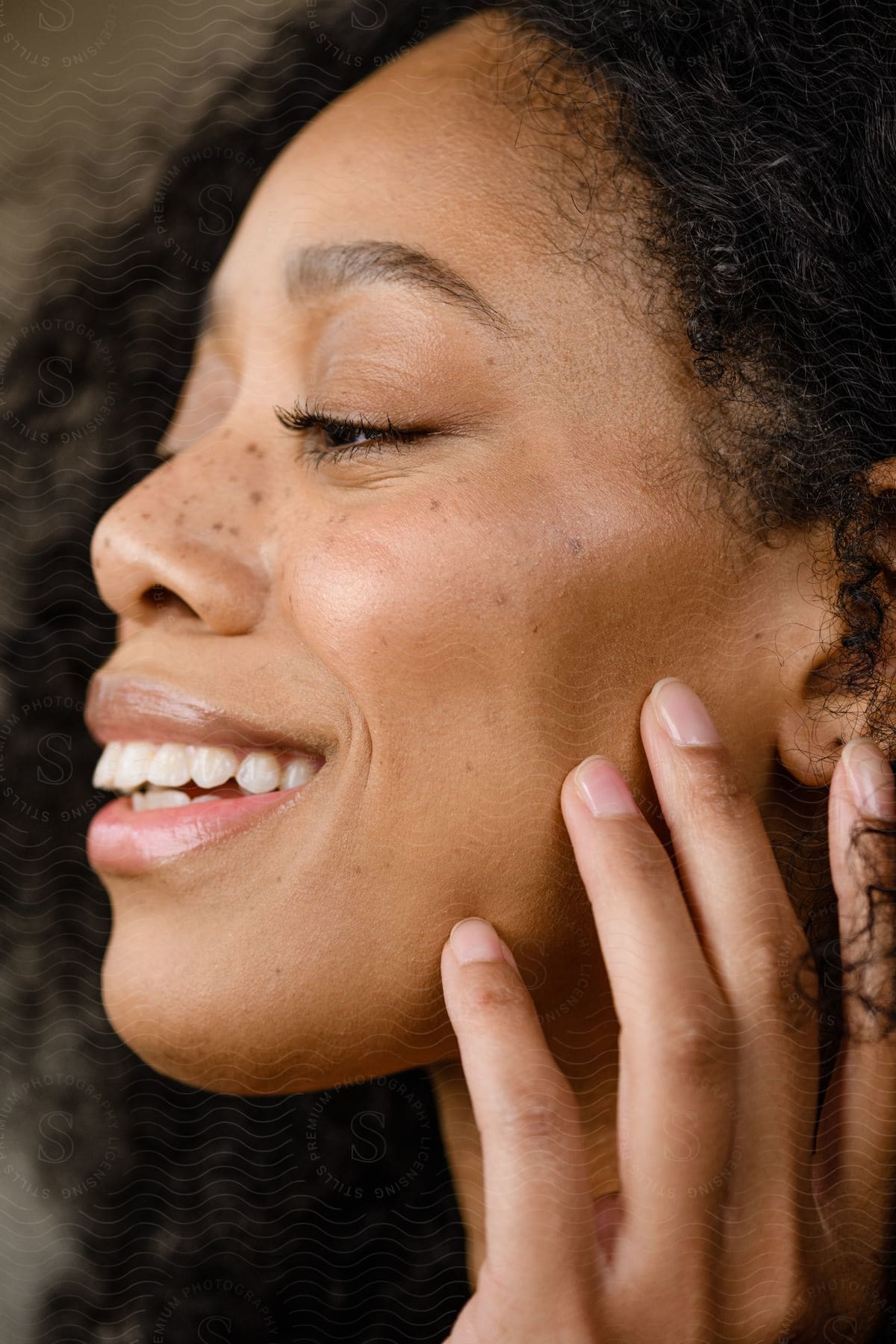 A face of a black woman who is smiling and her hand is on her cheek.