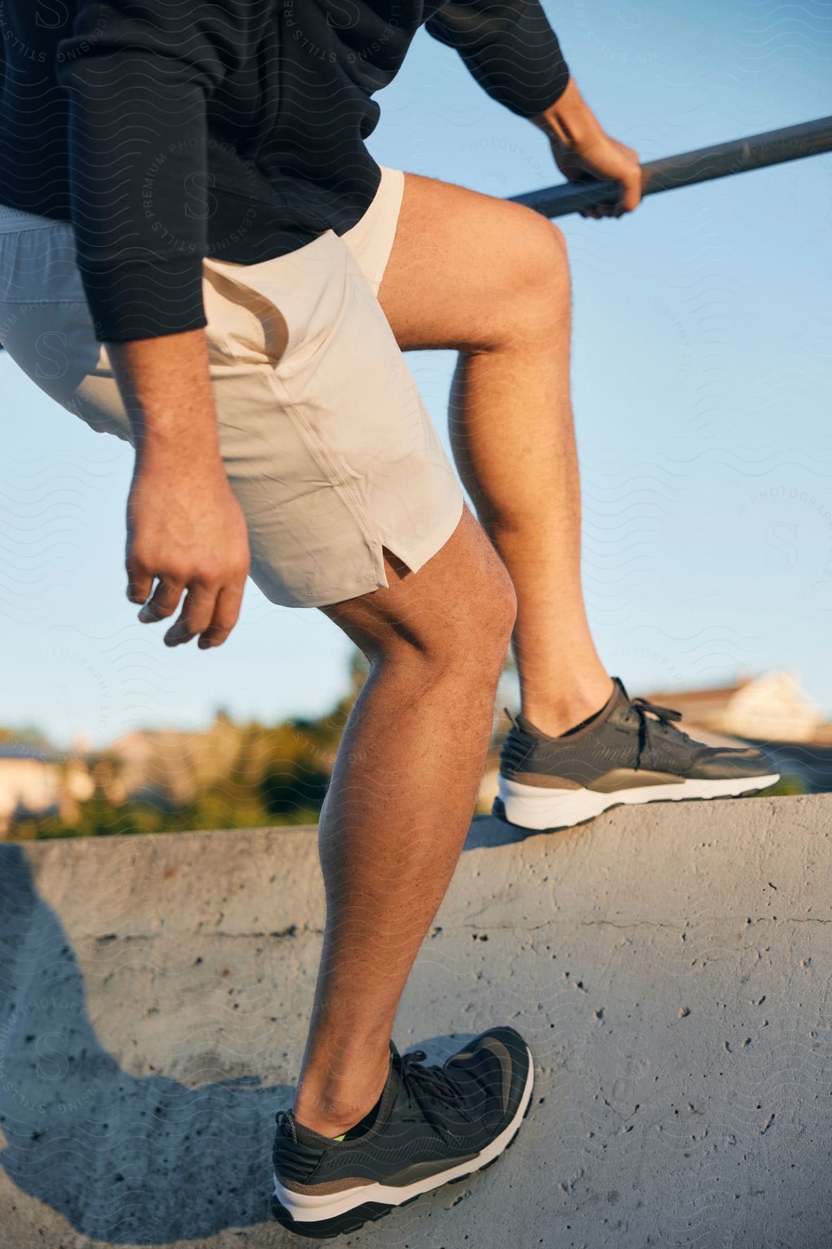 A man wearing shorts and sneakers posed at the top of a ramp holding a railing