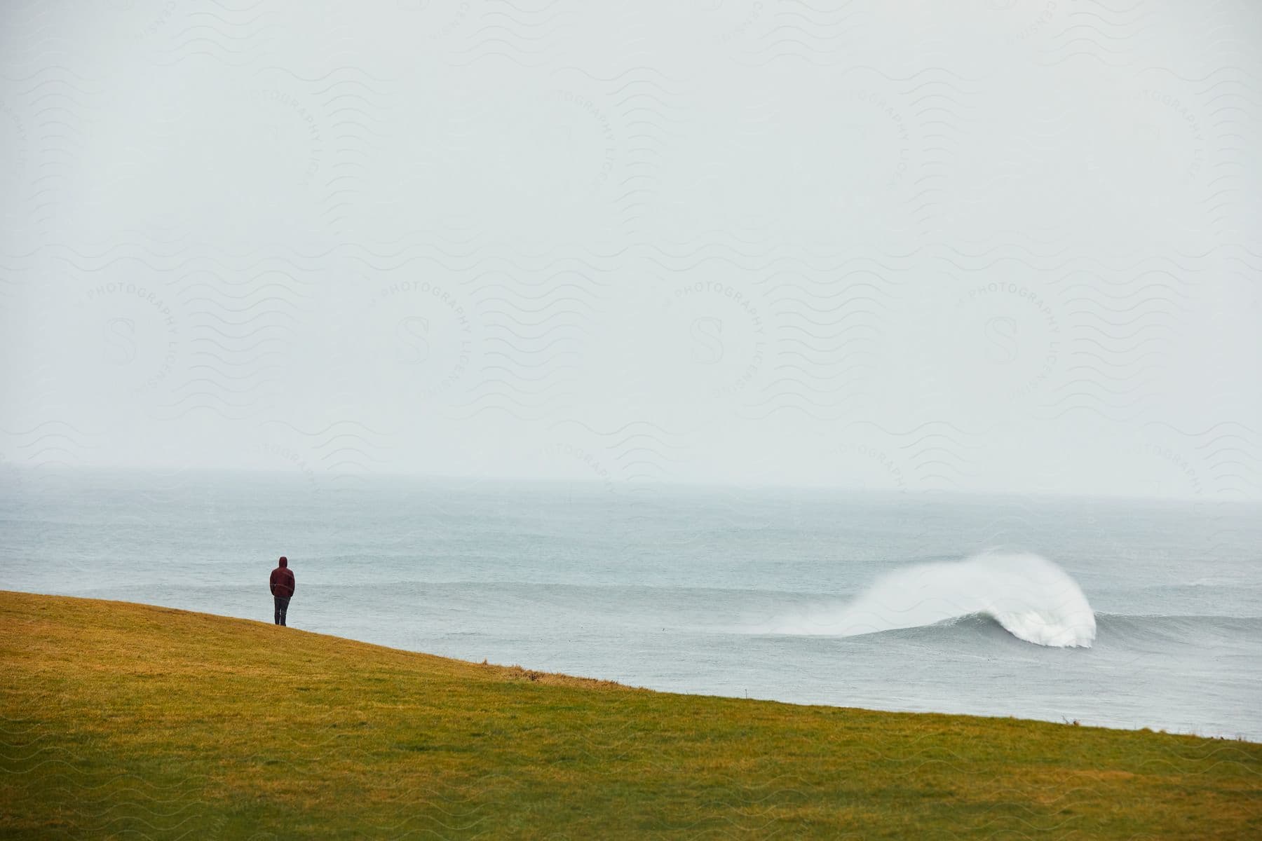 Man stands overlooking ocean with waves on a cloudy day.