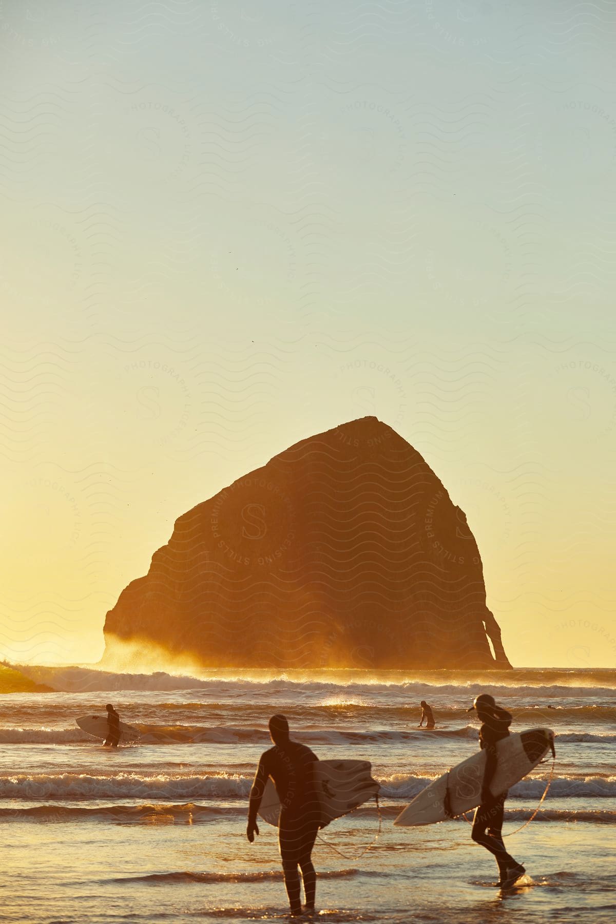 Four surfers are waiting for waves at sunset near the Haystack Rock at Cannon Beach.