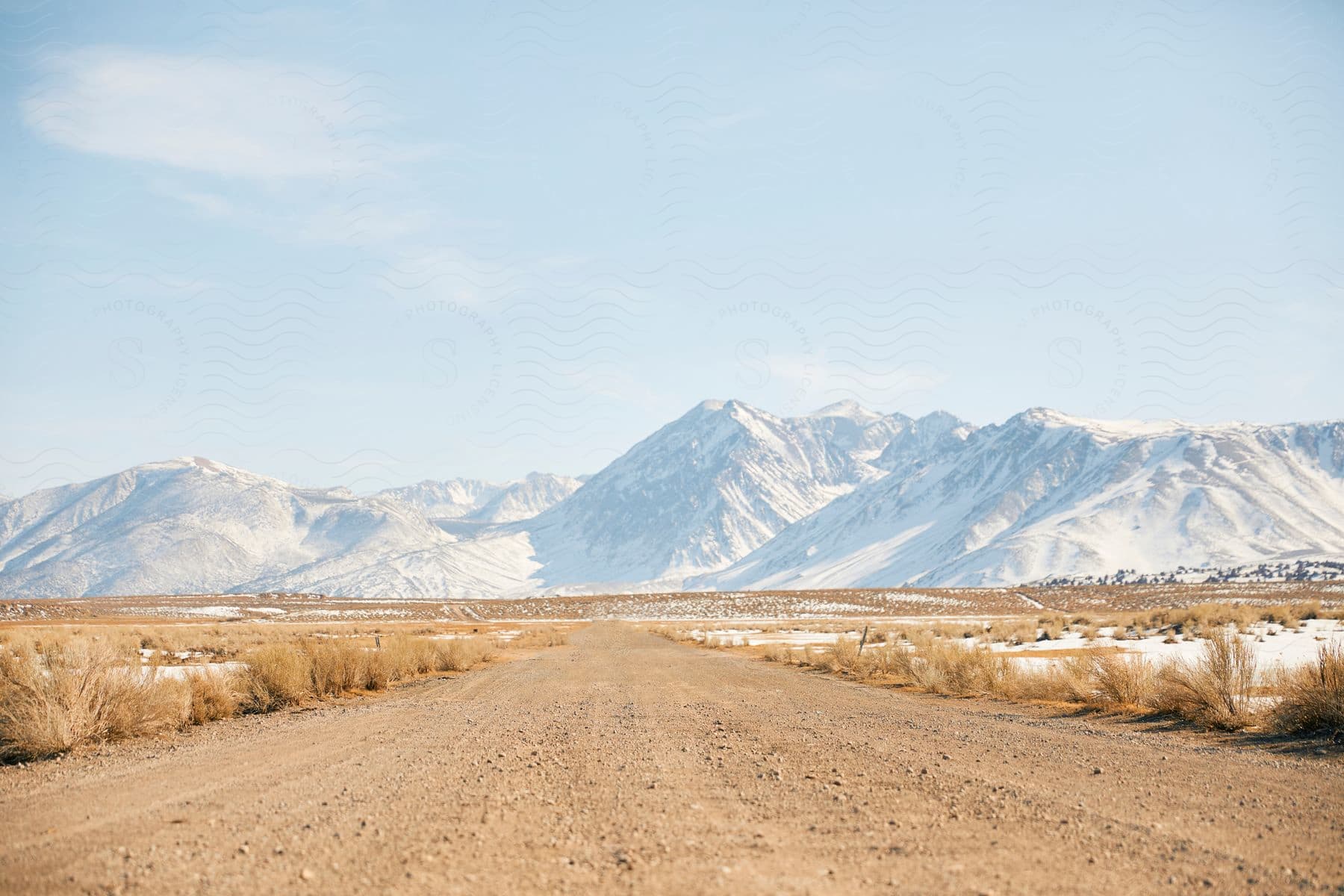 A dirt road running through the plains with snow covered mountains in the background.