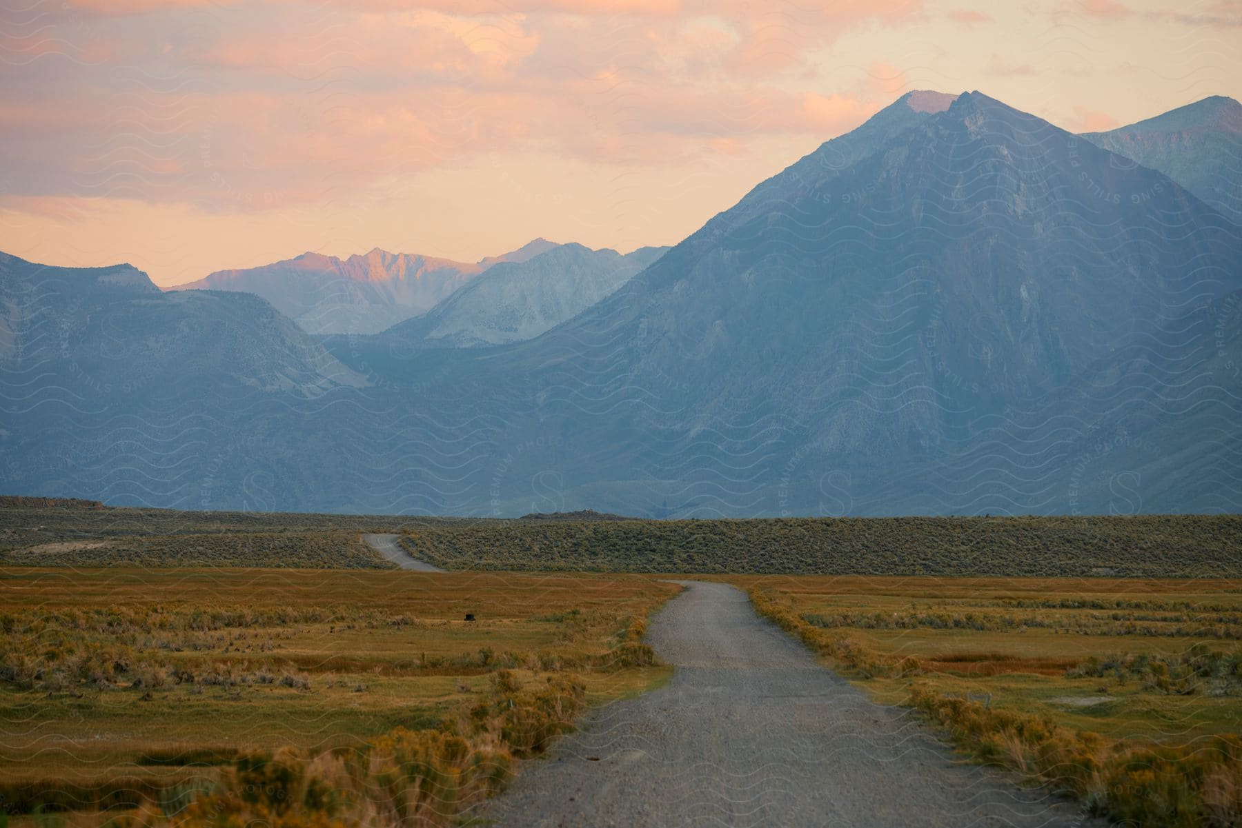 Cloudy sunset over mountain ridges with a road winding through the plains in the foreground.